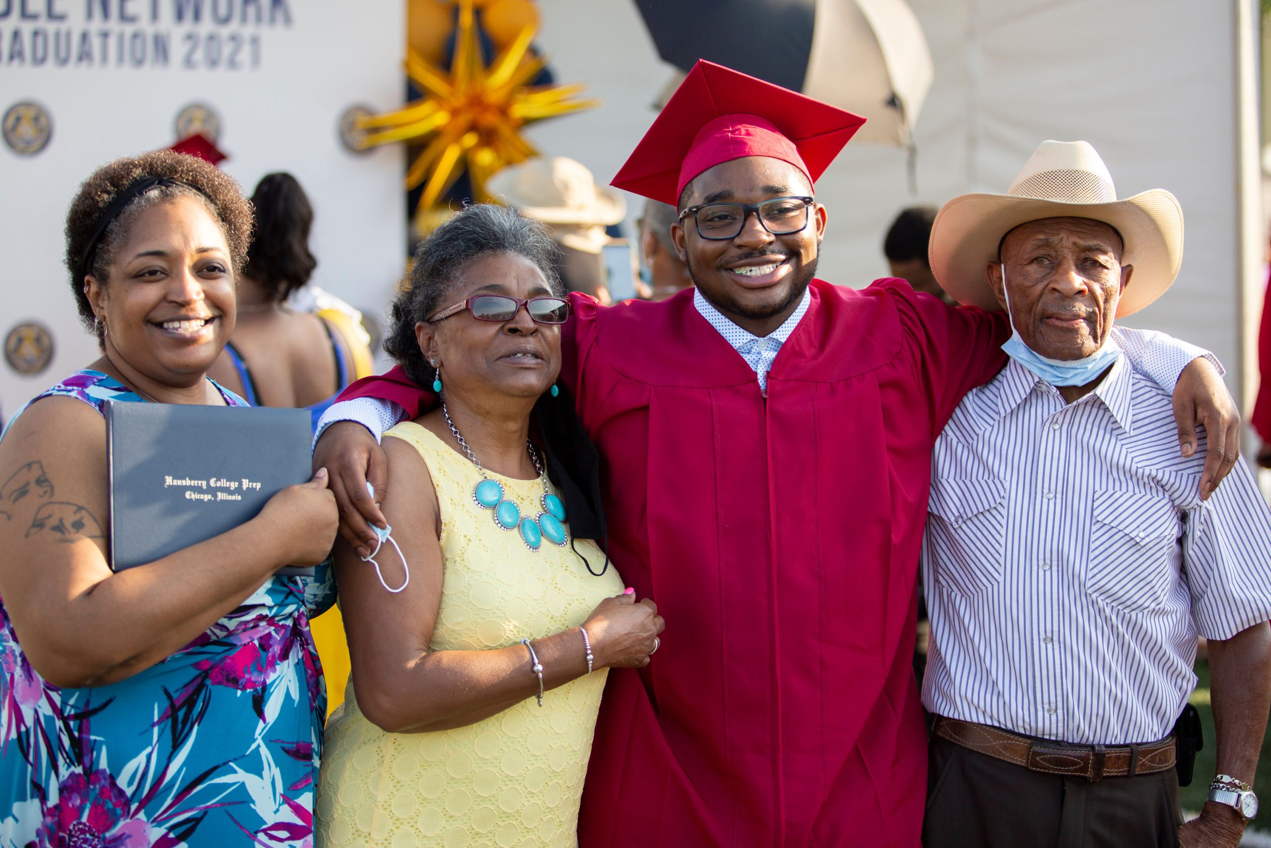 Photo shows a graduate from Hansberry College Prep in 2021, smiling with his family at graduation