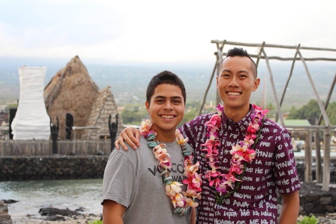 Photo shows JY Sun on the right with their former student Ka'ala on the left, in front of the beautiful landscape of Kailua-Kona, Hawai’i