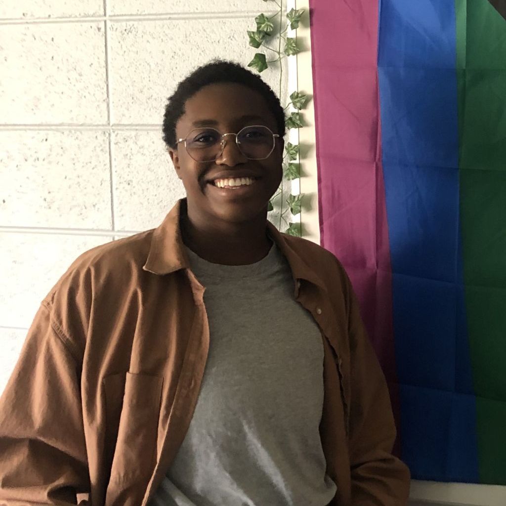 Image shows a portrait shot of Mx. T, a teacher at Baker College Prep and leader of the LGBTQ+ club, in front of a Pride flag