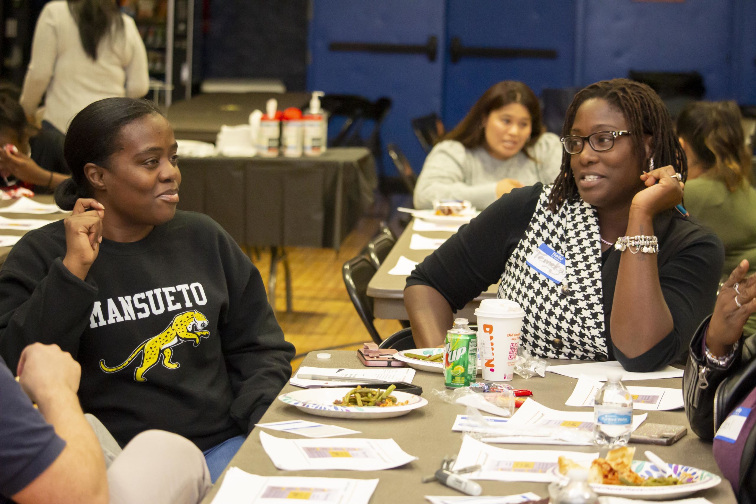 Photo shows two parents sitting at a table and talking during a Parent Leadership Series. Other Noble Schools parents can be seen at other tables in the background.
