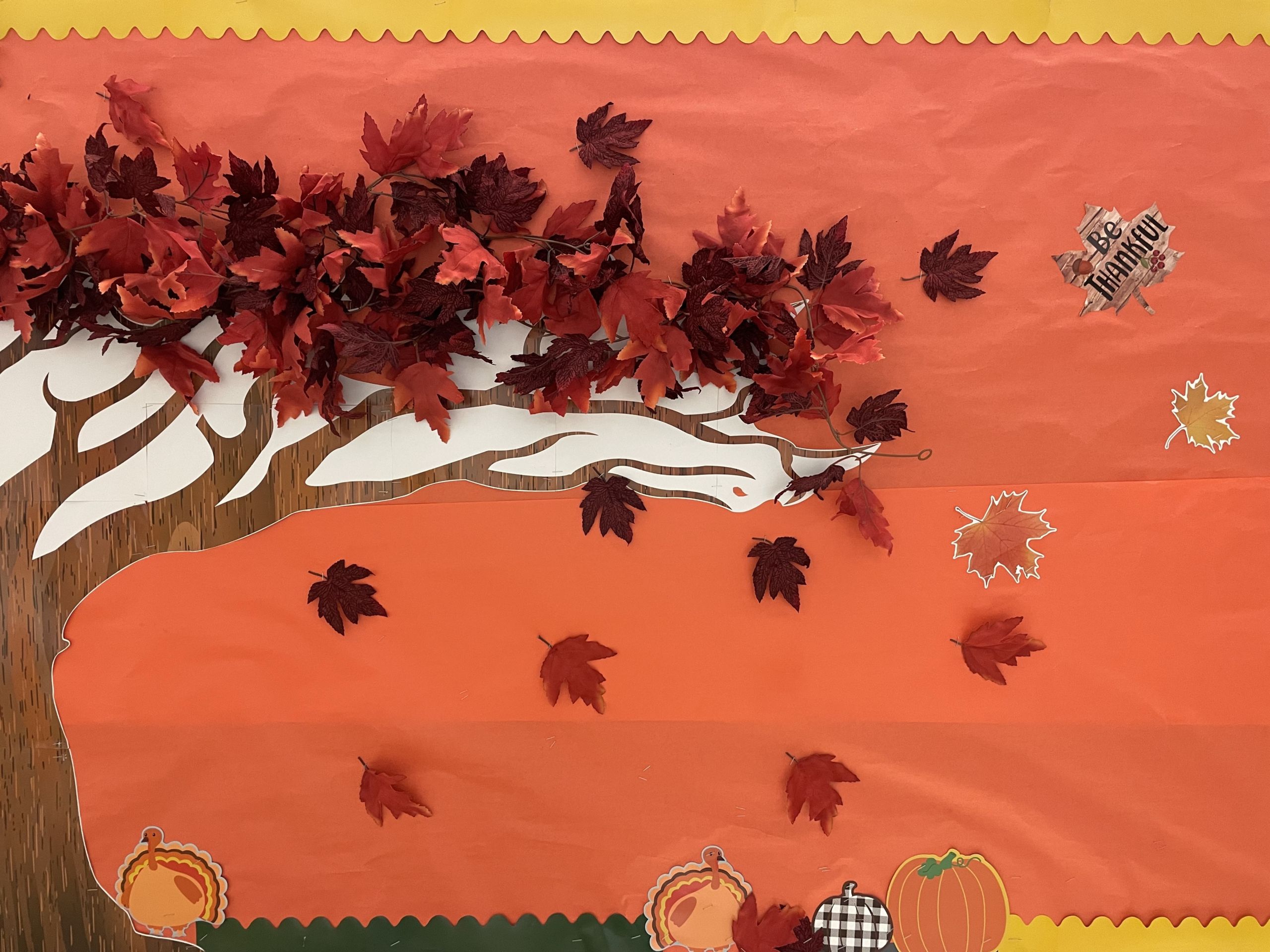 Image shows a bright orange bulletin board with a paper tree on it with colorful falling leaves.