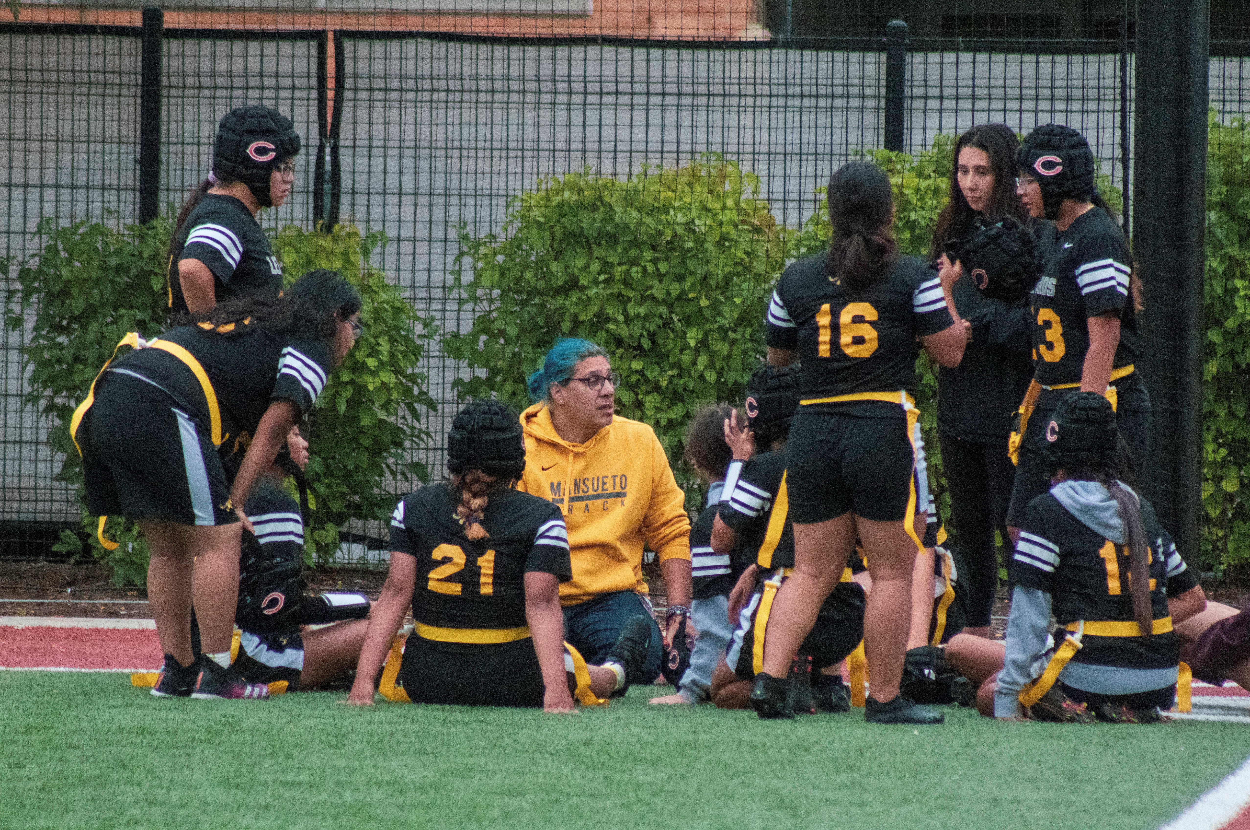 Image shows the Mansueto High Schools girls' flag football team gathered on the field with their coaches.