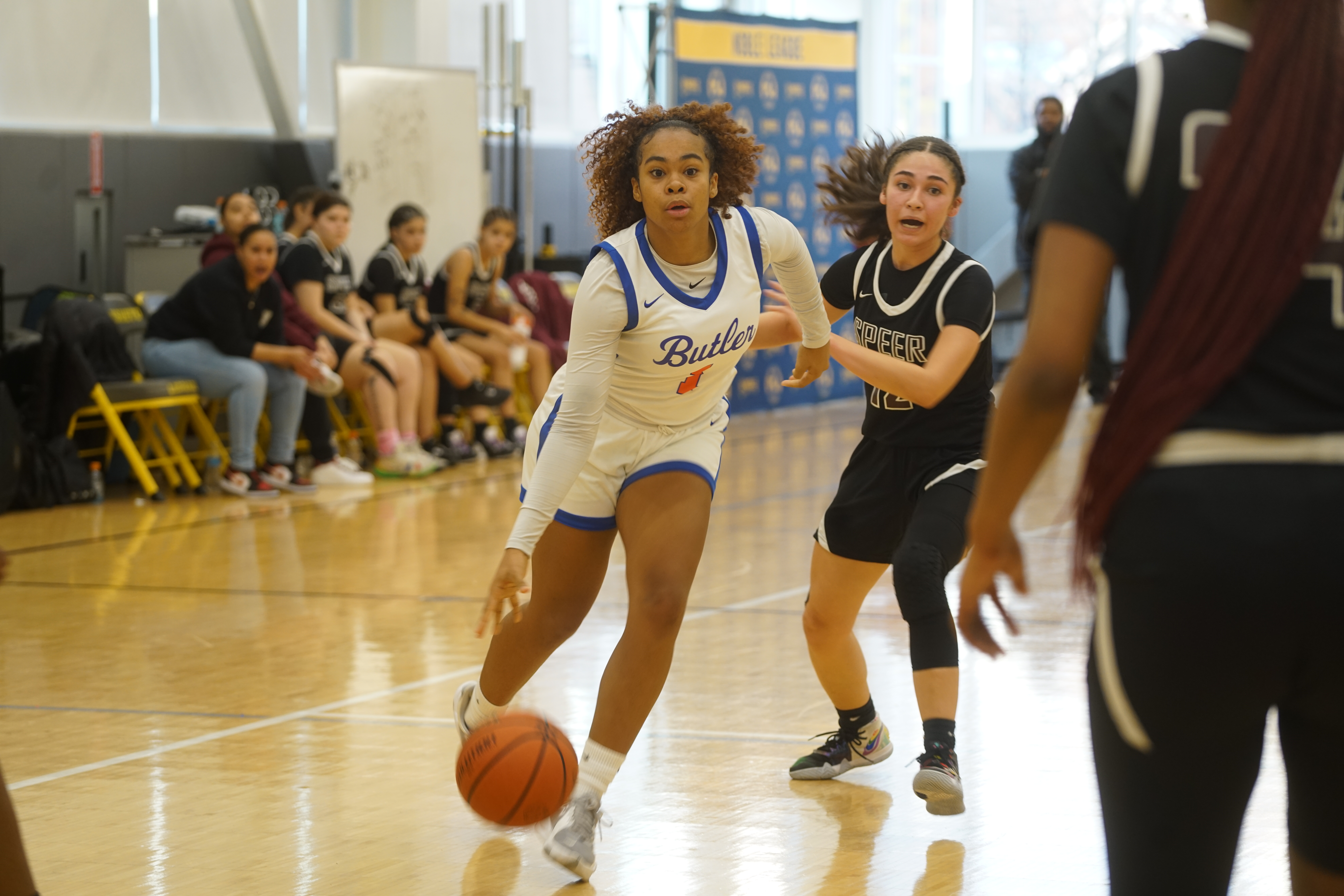 Xamiya playing in a game against a fellow Noble school team. She is in the center, dribbling the ball, as an opposing player closes in on her right.