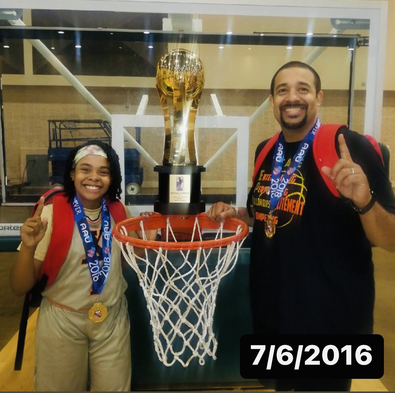 Photo shows Xamiya and her dad, smiling, and holding a giant trophy on top of a basketball hoop for the national championship that Xamiya's team won in 6th grade.