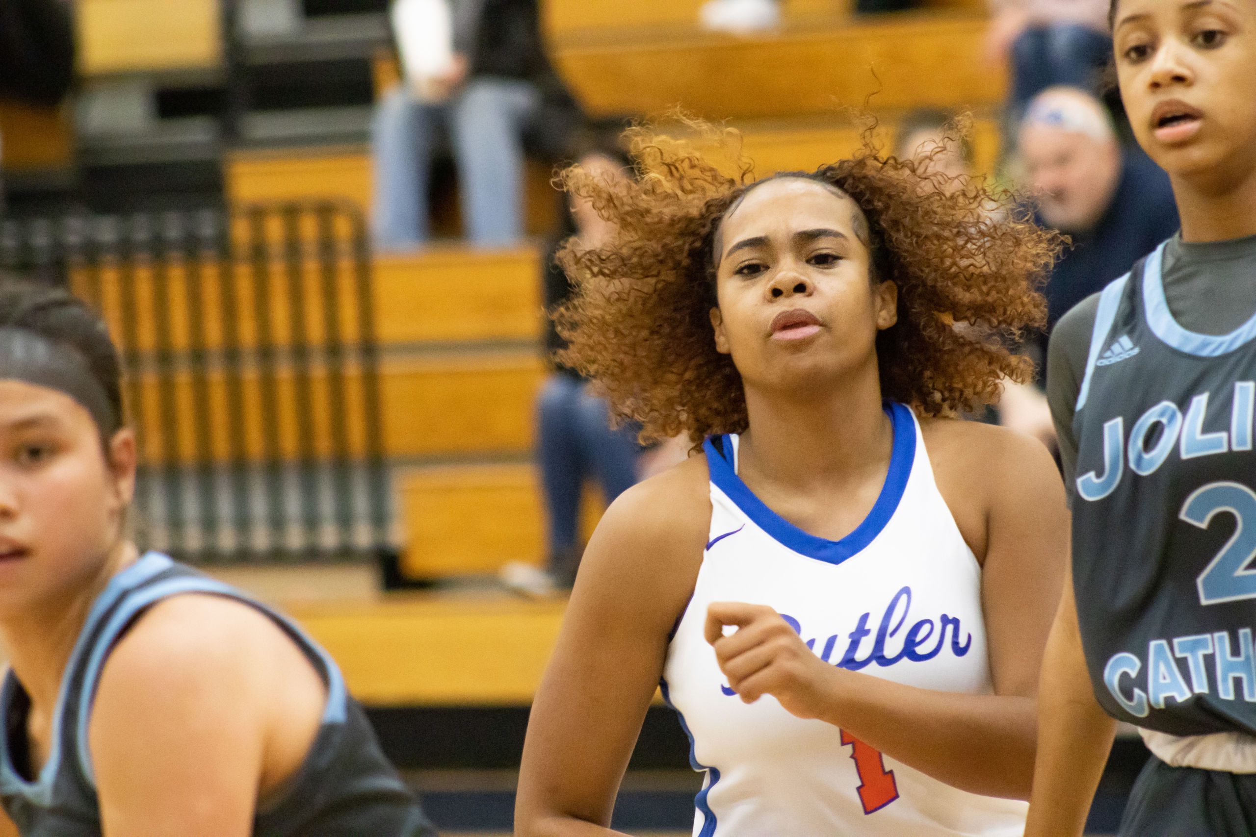 This photo shows a close-up of Xamiya running to the other end of the court with a face of concentration and effort. Opposing players are running on both sides of her.