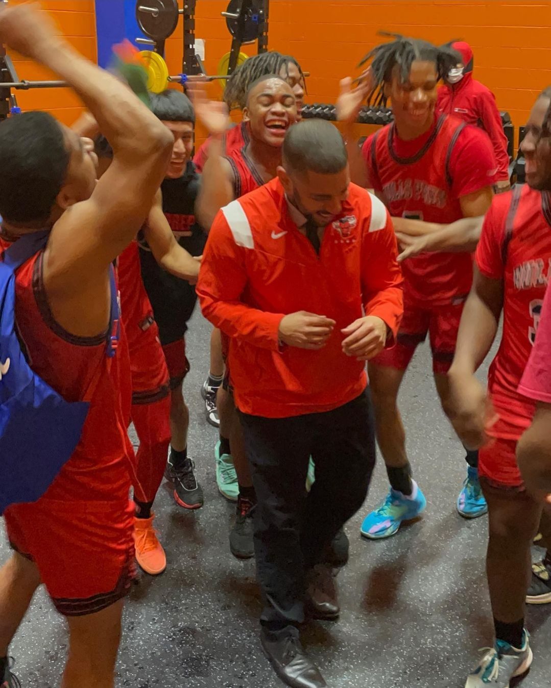 The Chicago Bulls College Prep basketball team celebrates their 100th win as Mr. Goldstein is cheering with them. The team crowds around Mr. Goldestein as he has his head down, smiling with them.