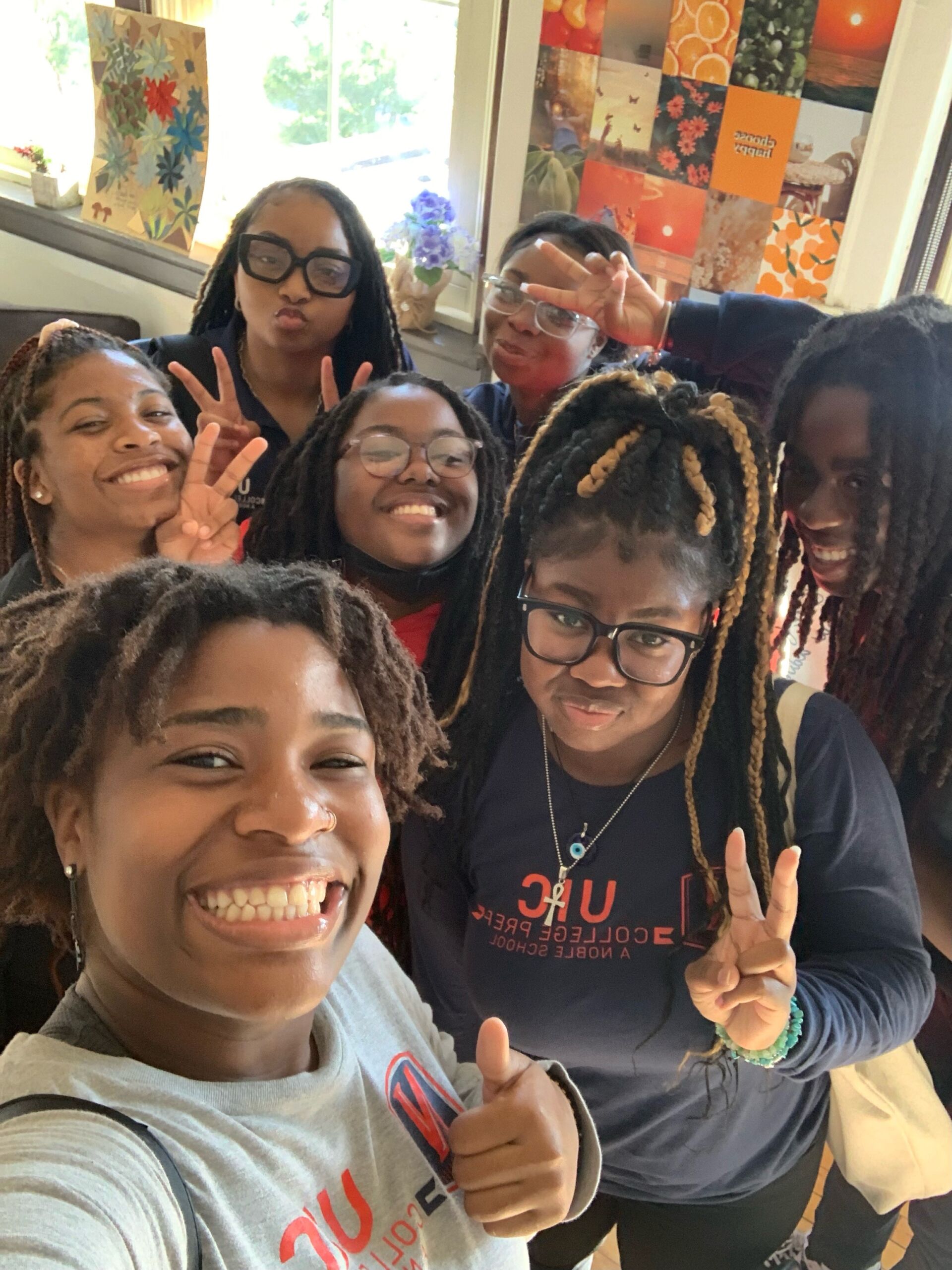Seven students are visible in the selfie. Some students are posing with peace signs while others are just smiling. One student has their thumbs up as their taking the selfie.