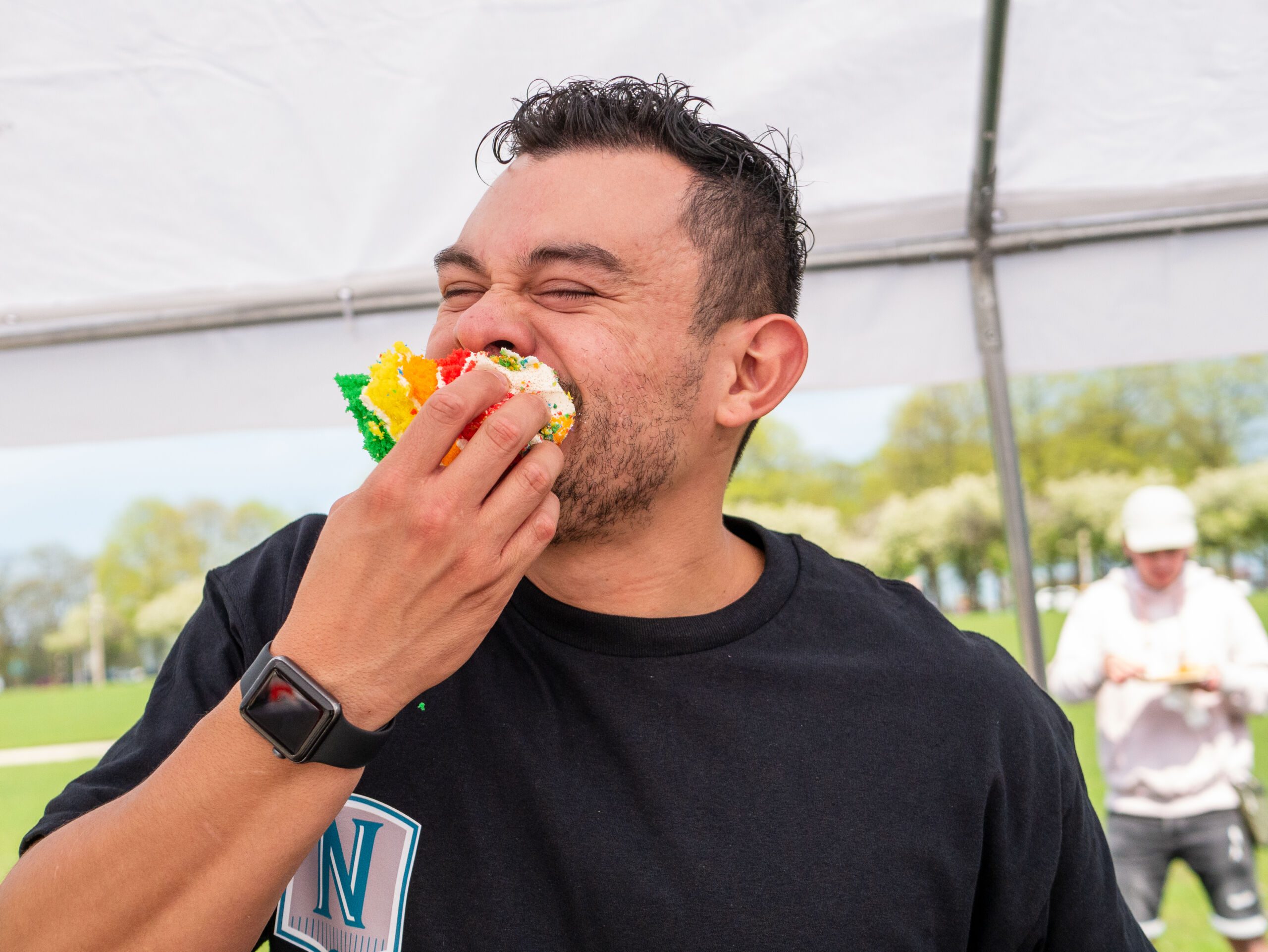 Photo of someone eating a cake slice at the carnival. Their eyes are closed. Their right hand is holding the slice as they eat it.