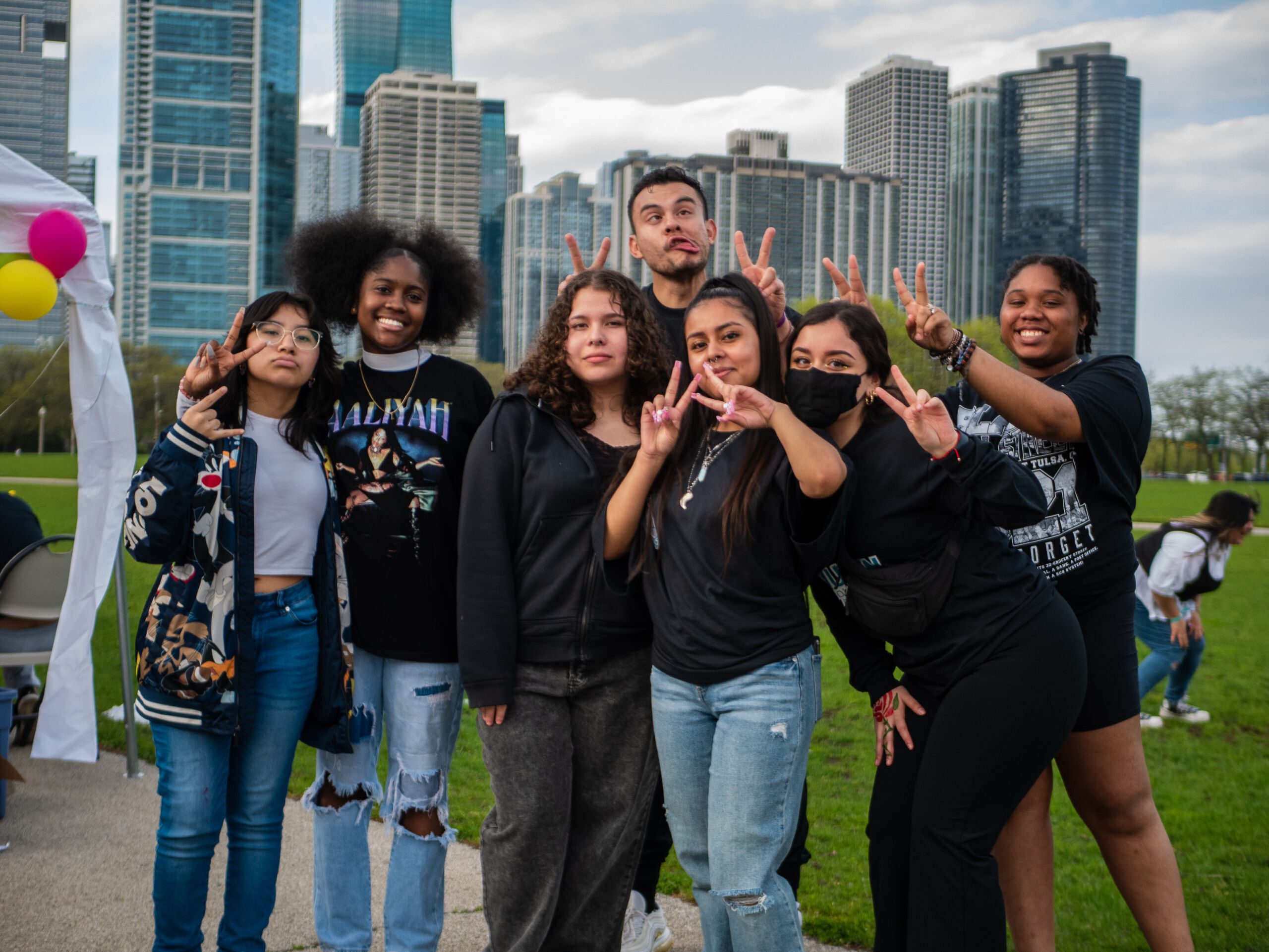 A group of students and others gather for a photo. Many are wearing black sweaters while others are wearing various types of clothing. They pose right in front of the Chicago skyline.