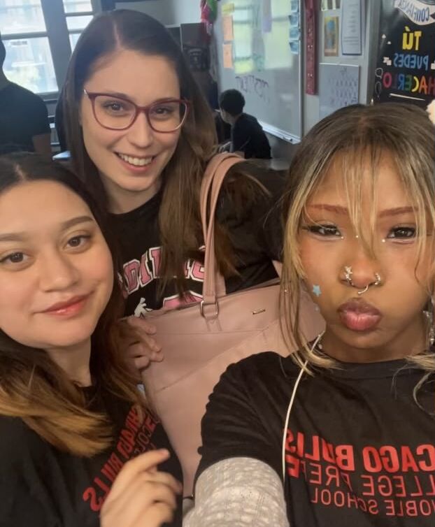 There is 3 people visible in the picture. From left to right, Jasmine, Ms. DiMonte, Life. Jasmine is posing with her advisor and friend. They are taking a selfie and smiling at the camera. They're in the classroom together.