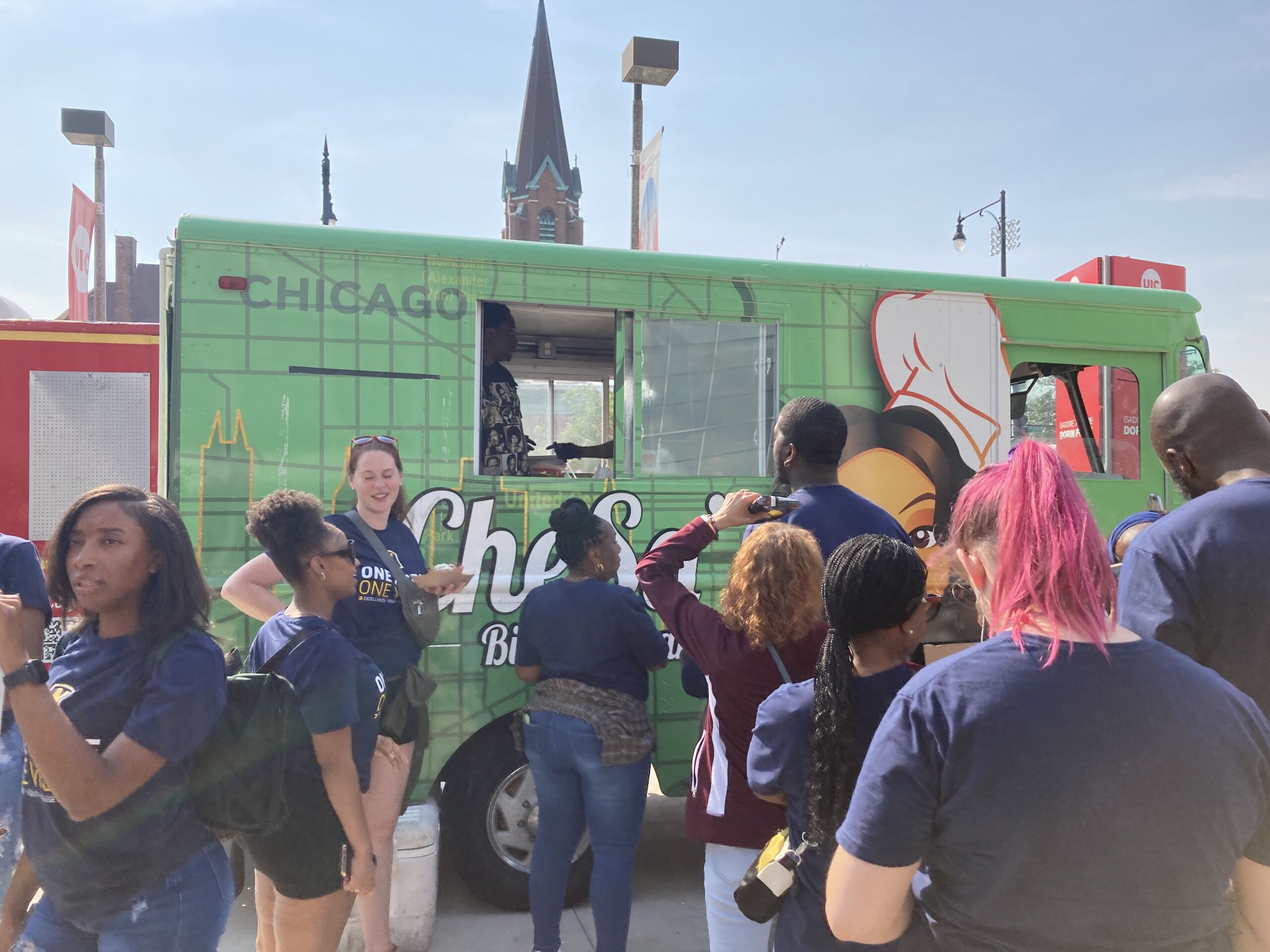 Photo shows a wide shot of the green Chesa's Bistro & Bar food truck as Noble Schools' staff members line up in front of it.