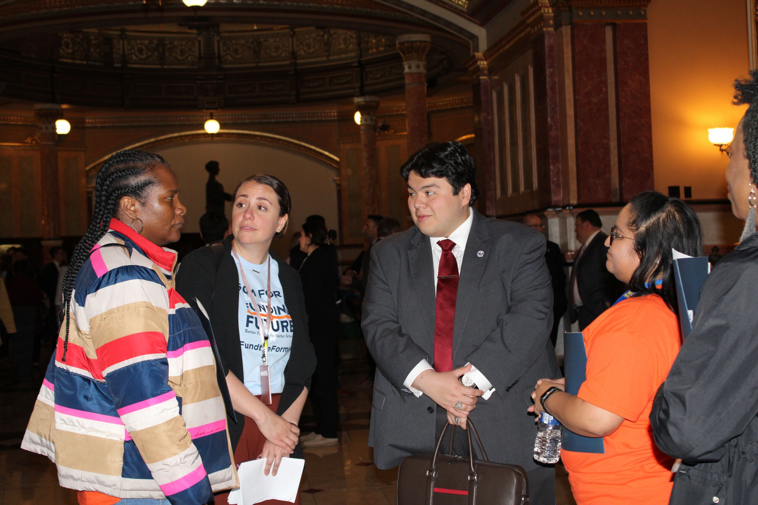Photo shows Noble Schools' parents and staff talking with Illinois State House representative in the hallways of the Illinois State Capitol building. From left to right, the people in the image are: Regina White, parent at DRW College Prep and The Noble Academy; Ellen Moiani, the Director of Government and Community Affairs at Noble Schools; representative, , and