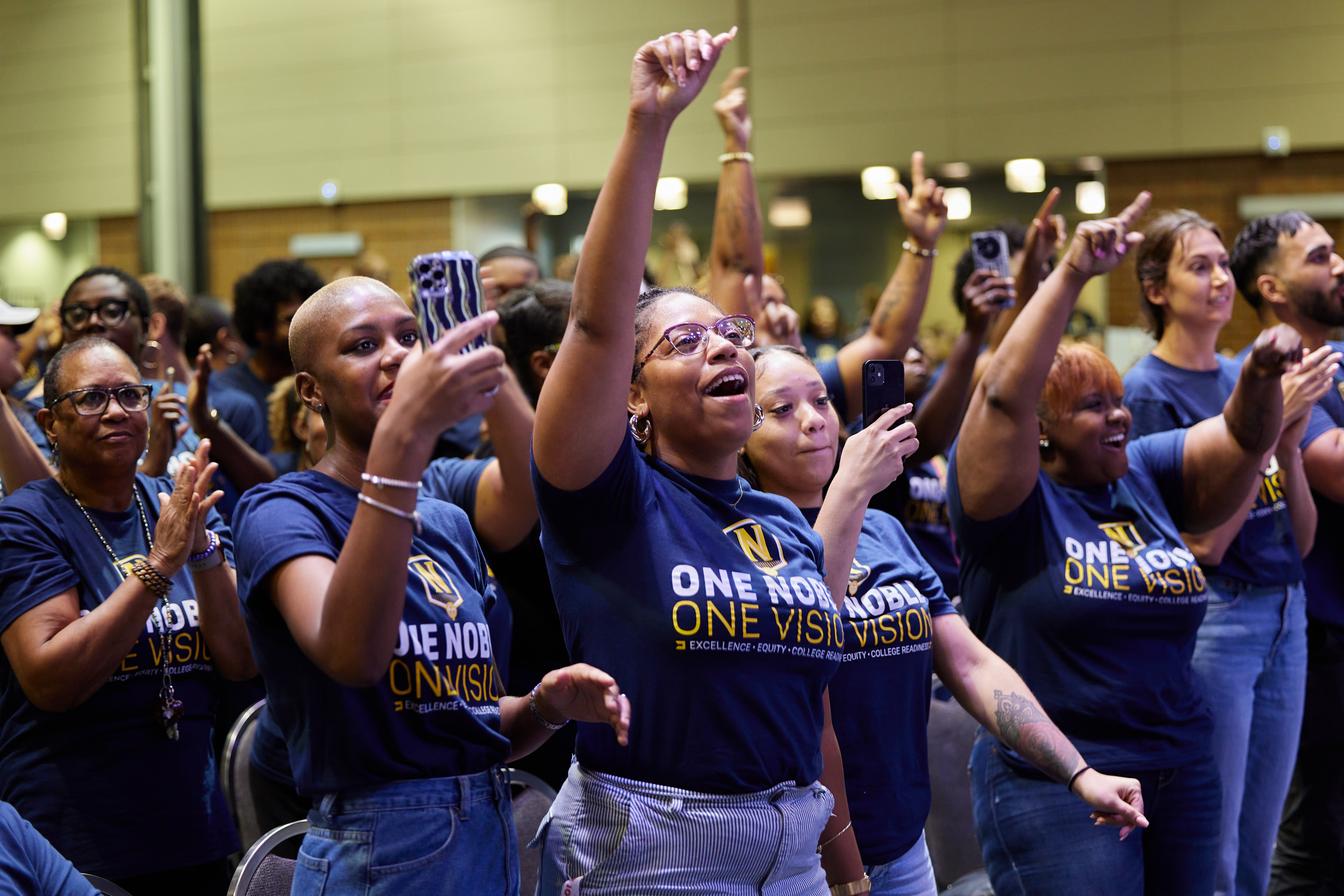 Photo shows a close-up of a group of Noble staff members who are cheering on and filming the Hansberry dance team as they perform. Many have their hands raised or are clapping.