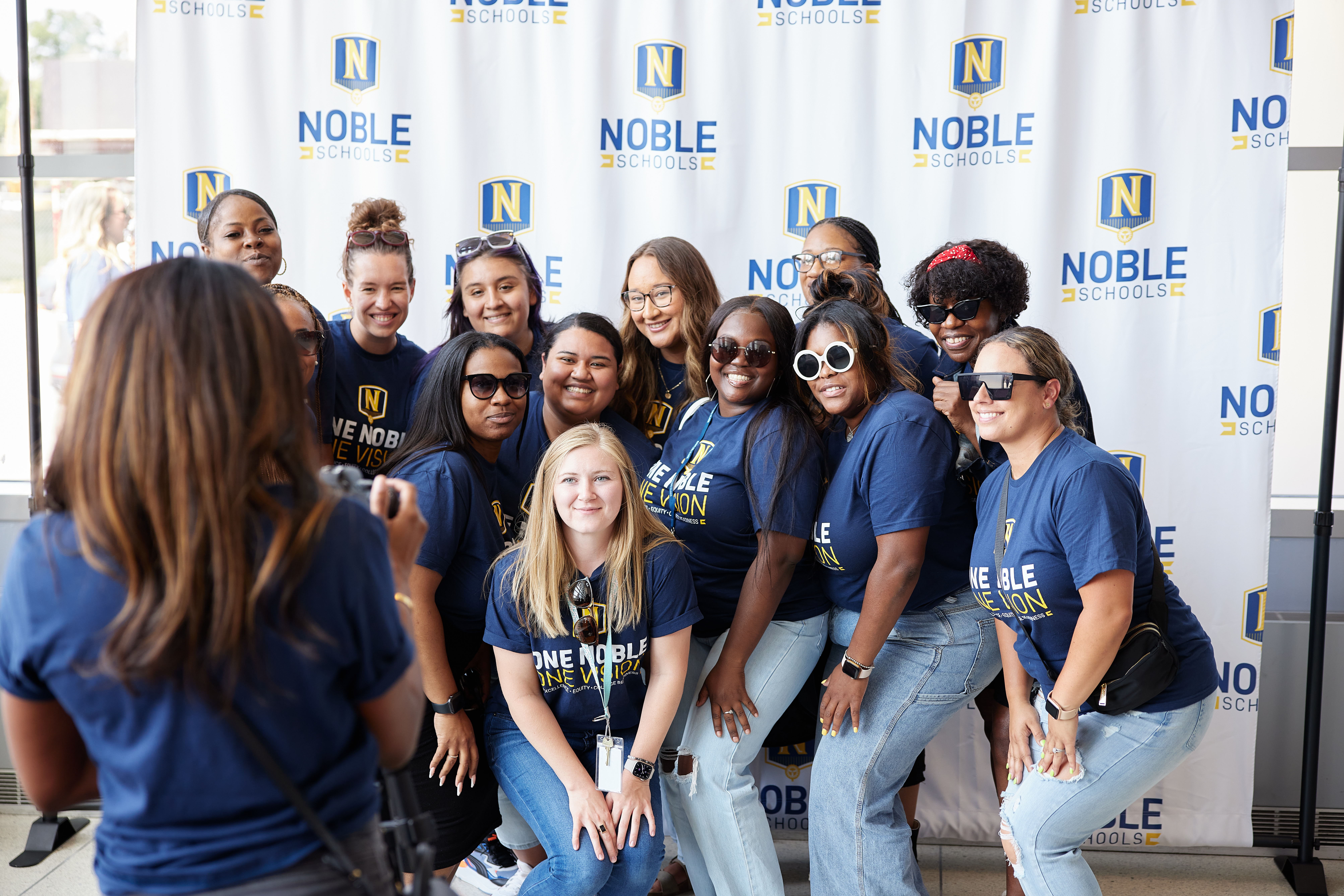 Photo shows a group of Noble Schools' staff members posing in front of a backdrop with the Noble Schools'