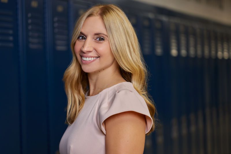 professional photo of Arrigo smiling with lockers in the background. she is wearing a soft pink top