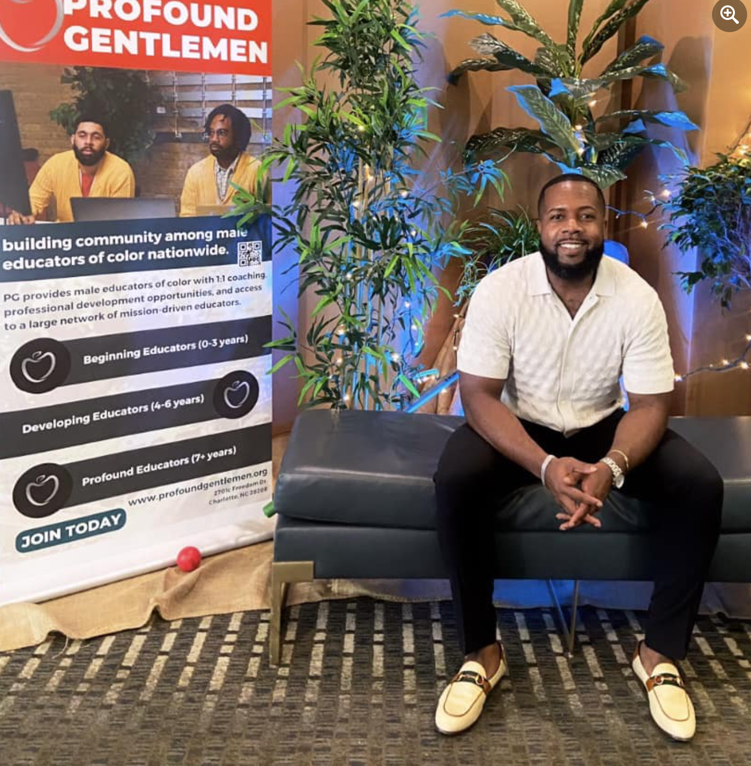 Photo shows Principal Brian Riddick sitting on a bench next to the sign about "Profound Gentlemen", a program for building community among male educators of color nationwide. He is smiling at the camera.