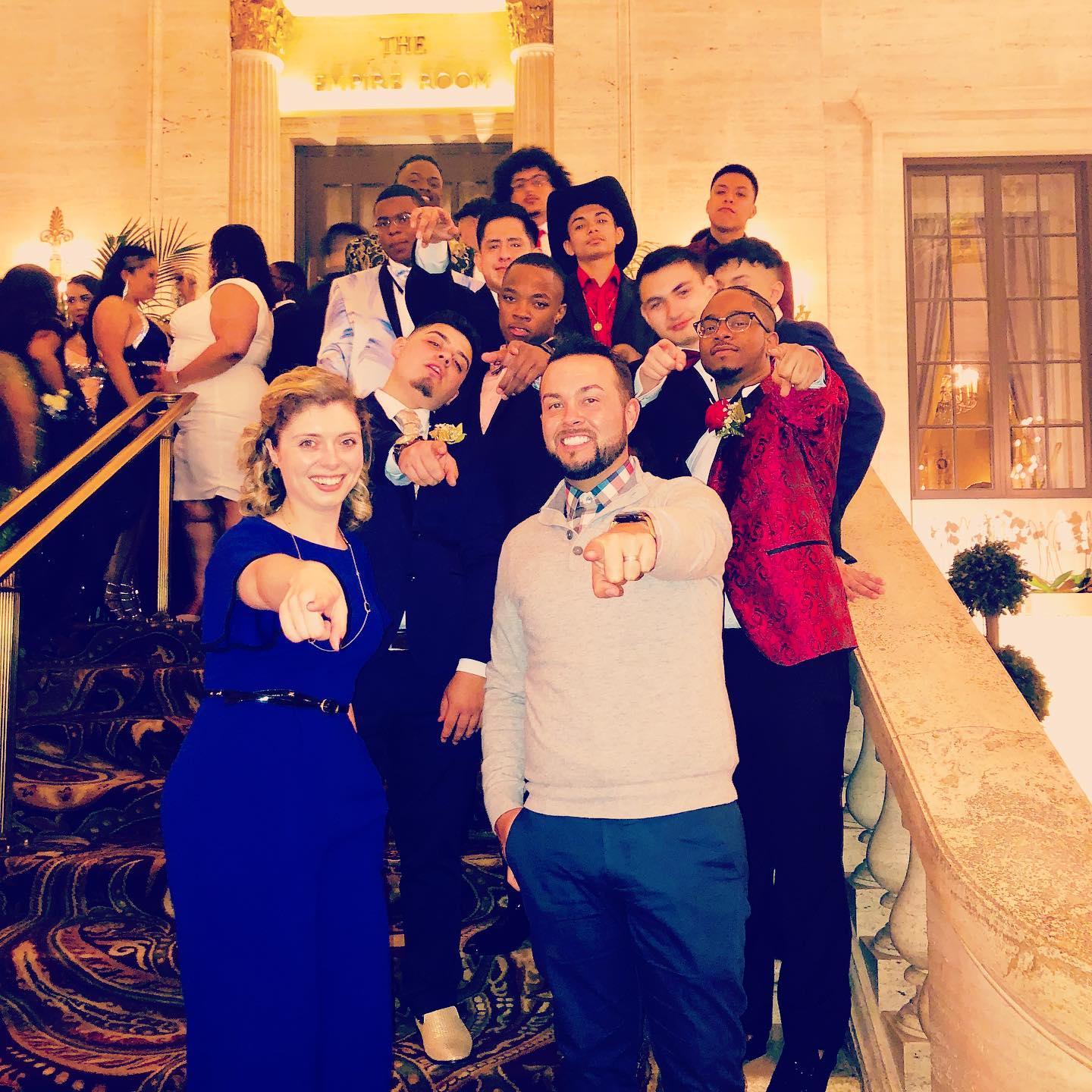 Photo of Chase Johnson-Espinoza and other party attendees on the stairs at a formal event. They are all pointing at the camera in a humorous way.