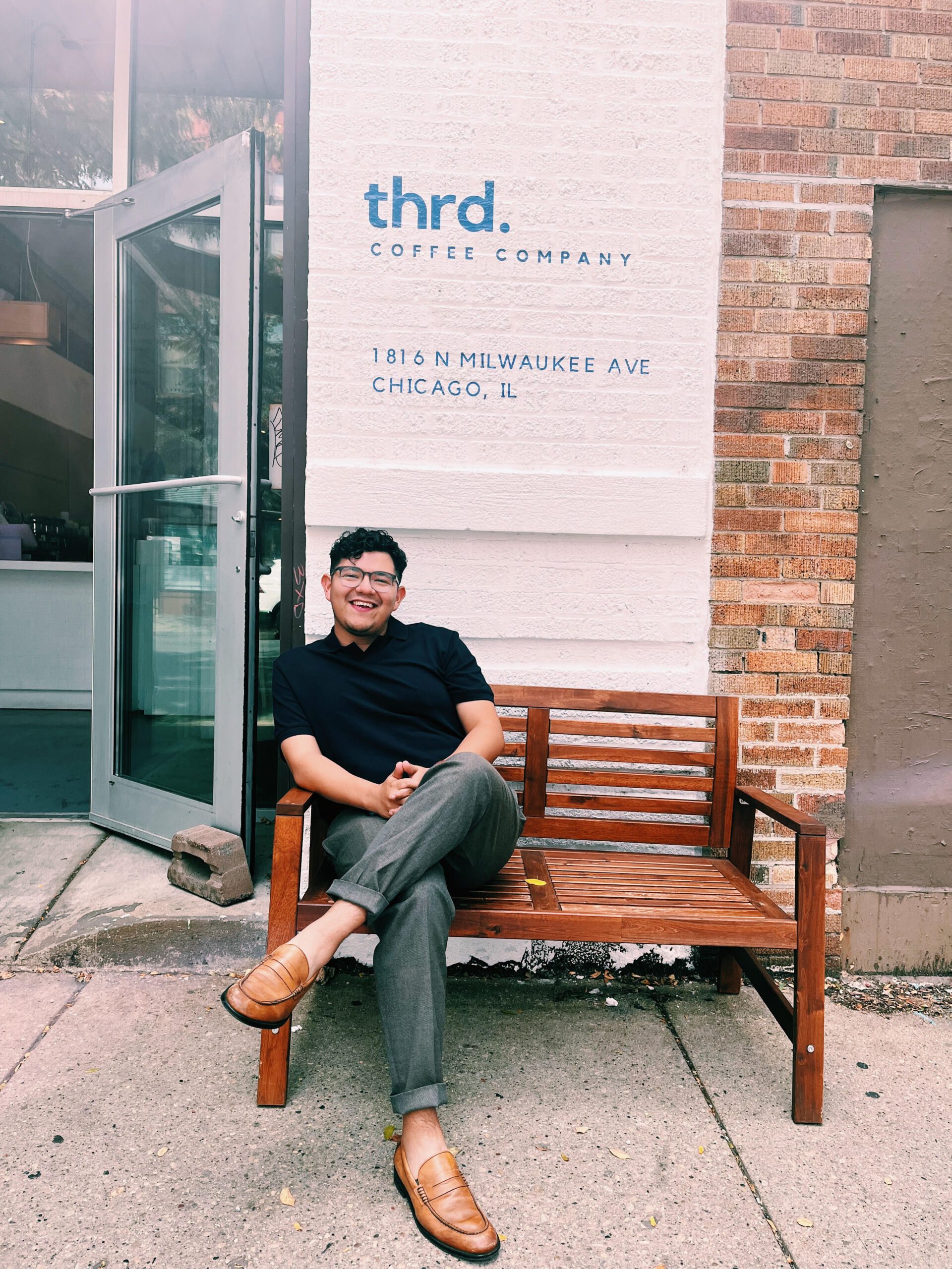 Image shows Raoul Adwan, a UIC College Prep alum, sitting on a bench in front of his coffee shop location, Thrd Coffee Company.