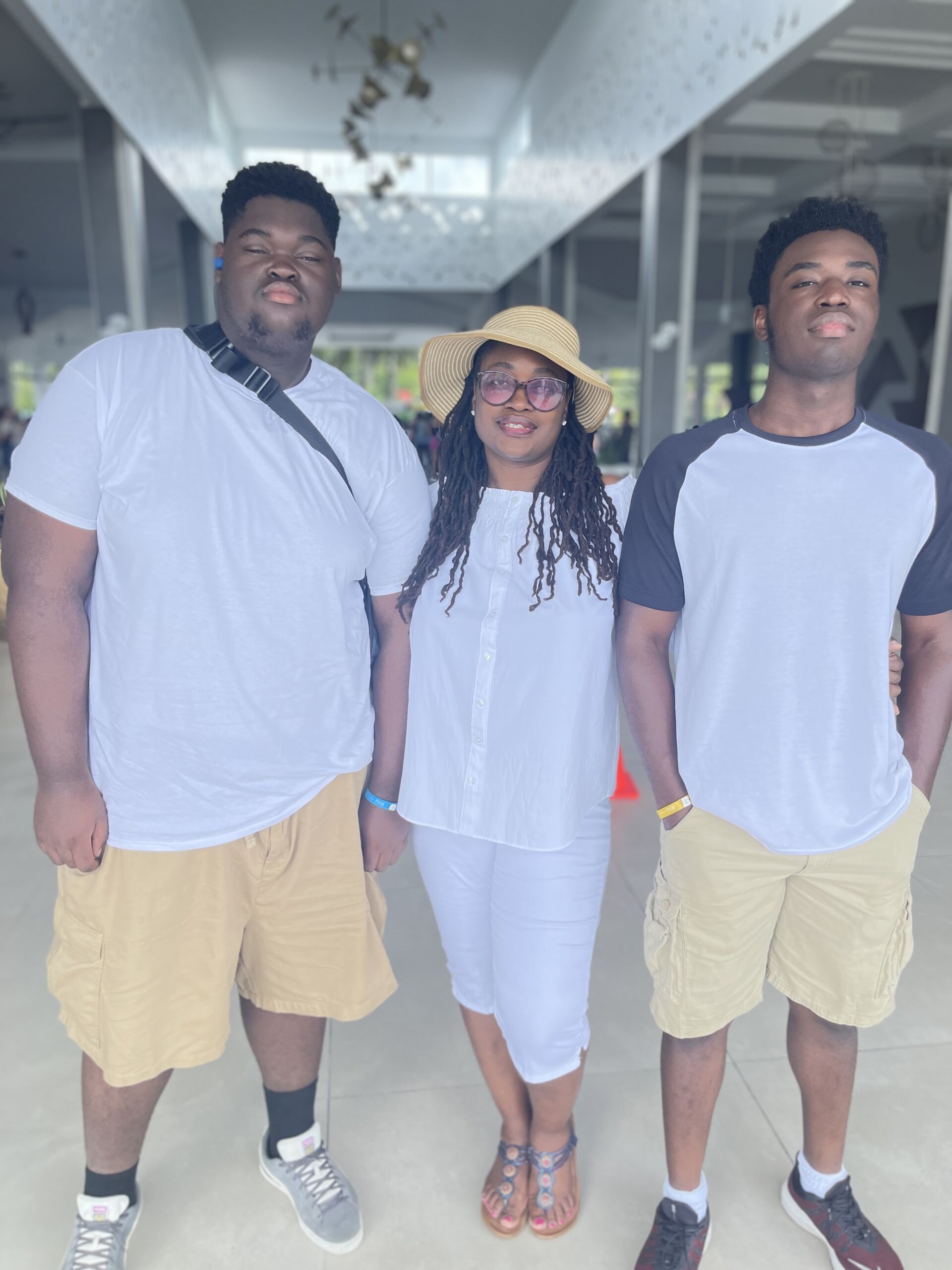 Photo shows Tina Ellis, principal of DRW College Prep, between her two grown up sons. They are all wearing summer clothes and standing in a long non-descript hallway.