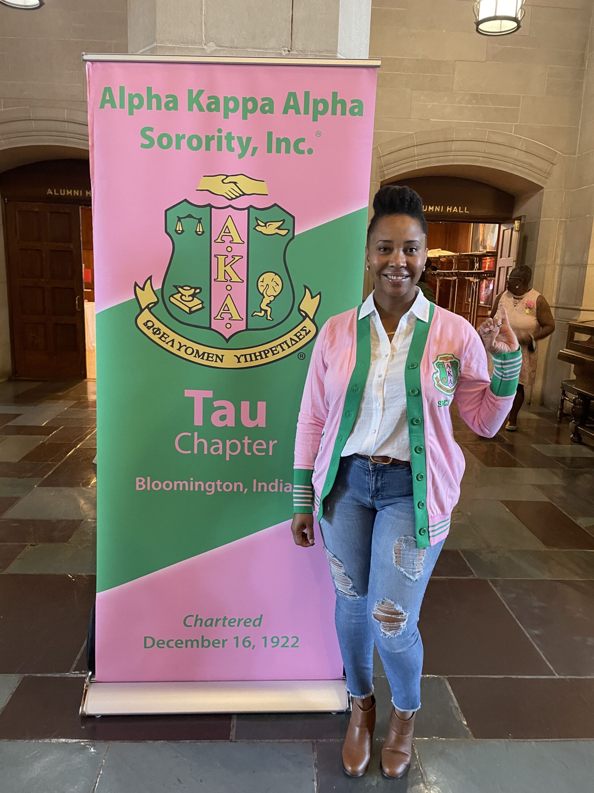 bennett posed in a pink and green cardigan, white button up, and jeans with her pinky up representing her sorority, Alpha Kappa Alpha.