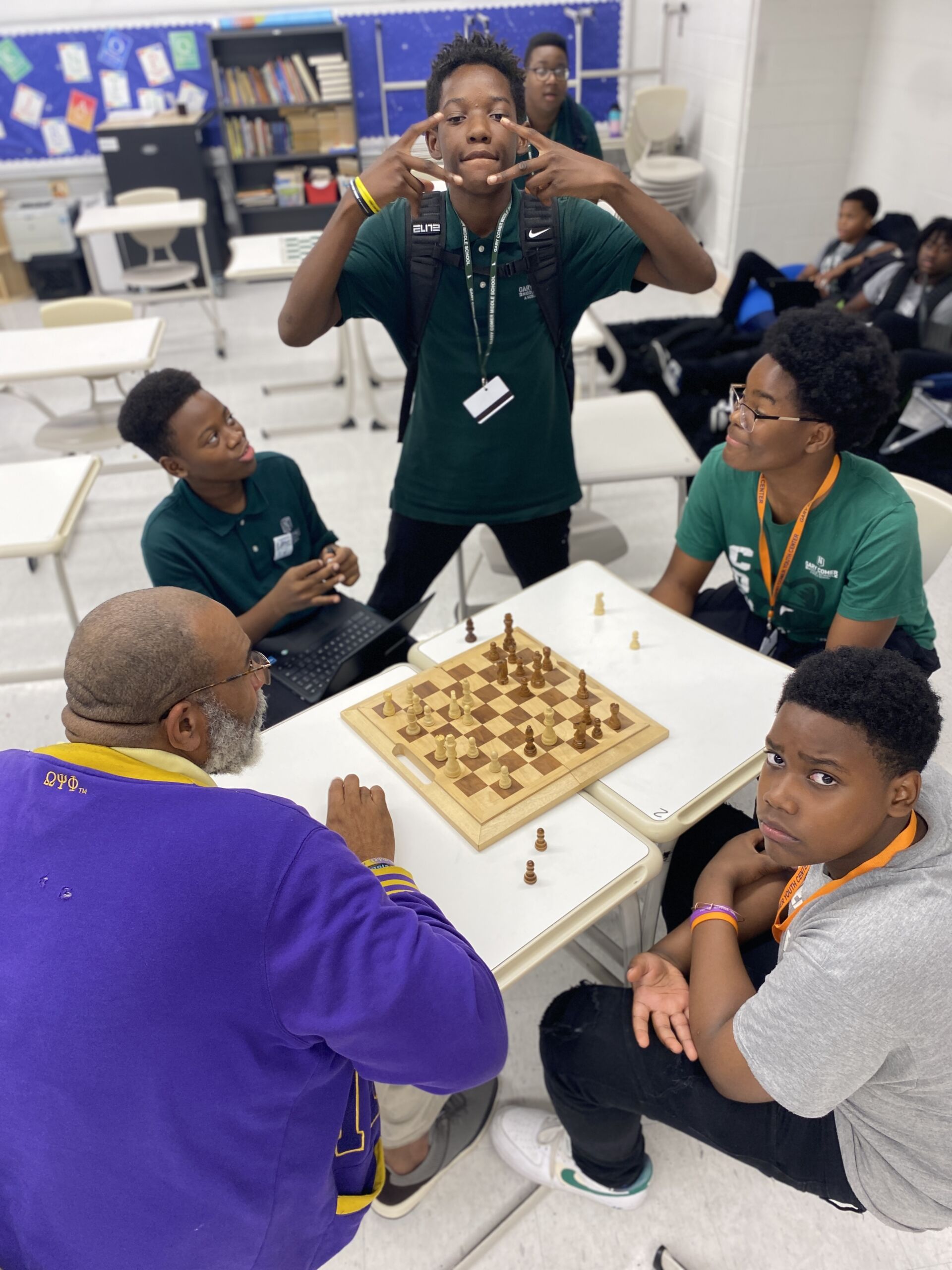 Mr. Brady, Octavius, Khari, and Trenton sit together and play chess. Just throws up two peace signs as he poses for the picture.