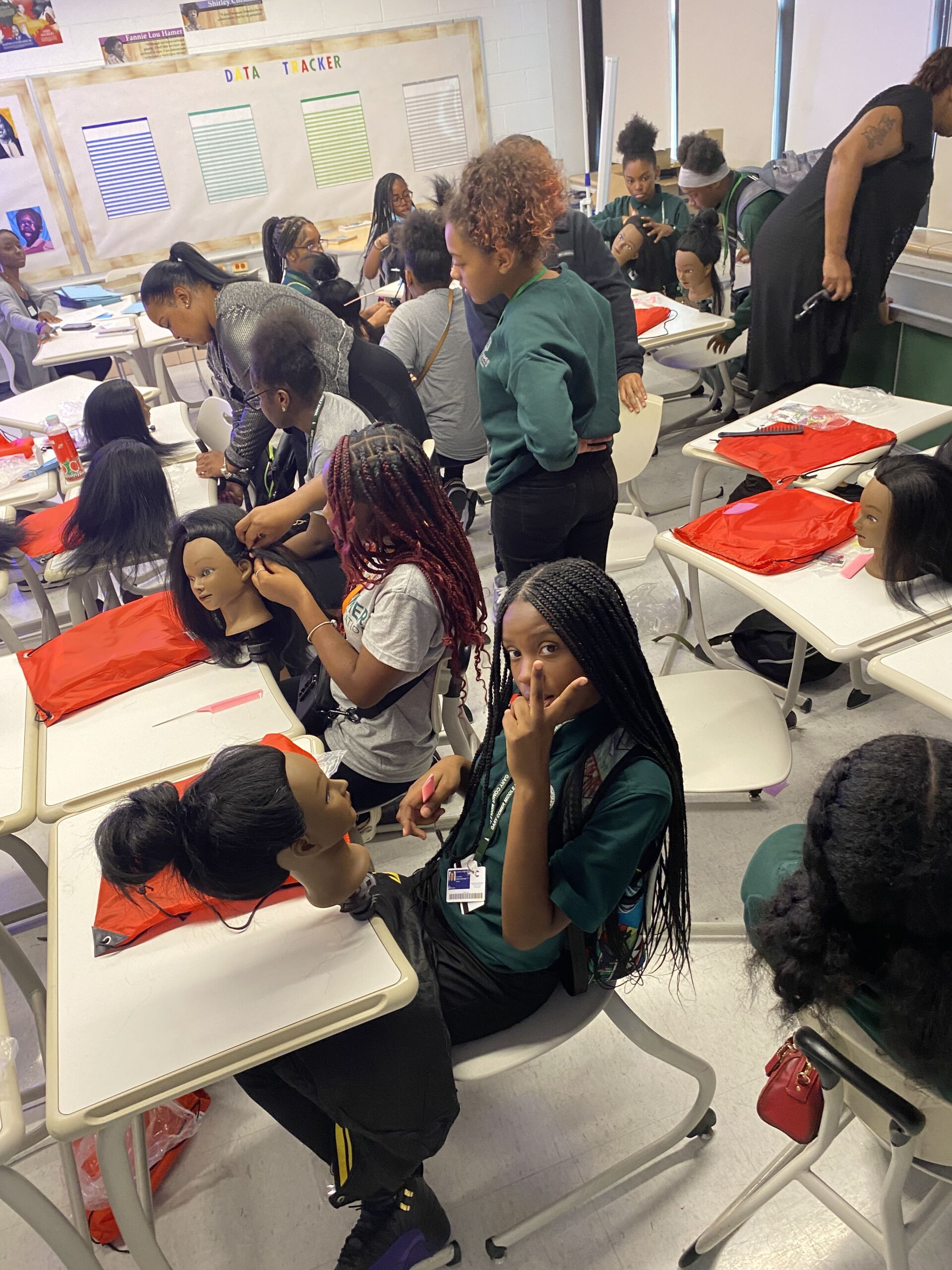 Gary Comer students sitting at desks braiding mannequin head hair. Some students are working together and talking.