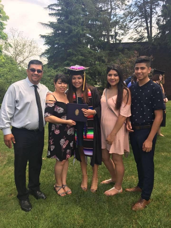In this photo, you can see Sbeydi Gonzalez standing with her family outside after her college graduation ceremony. She is wearing her college graduation robes and cap.