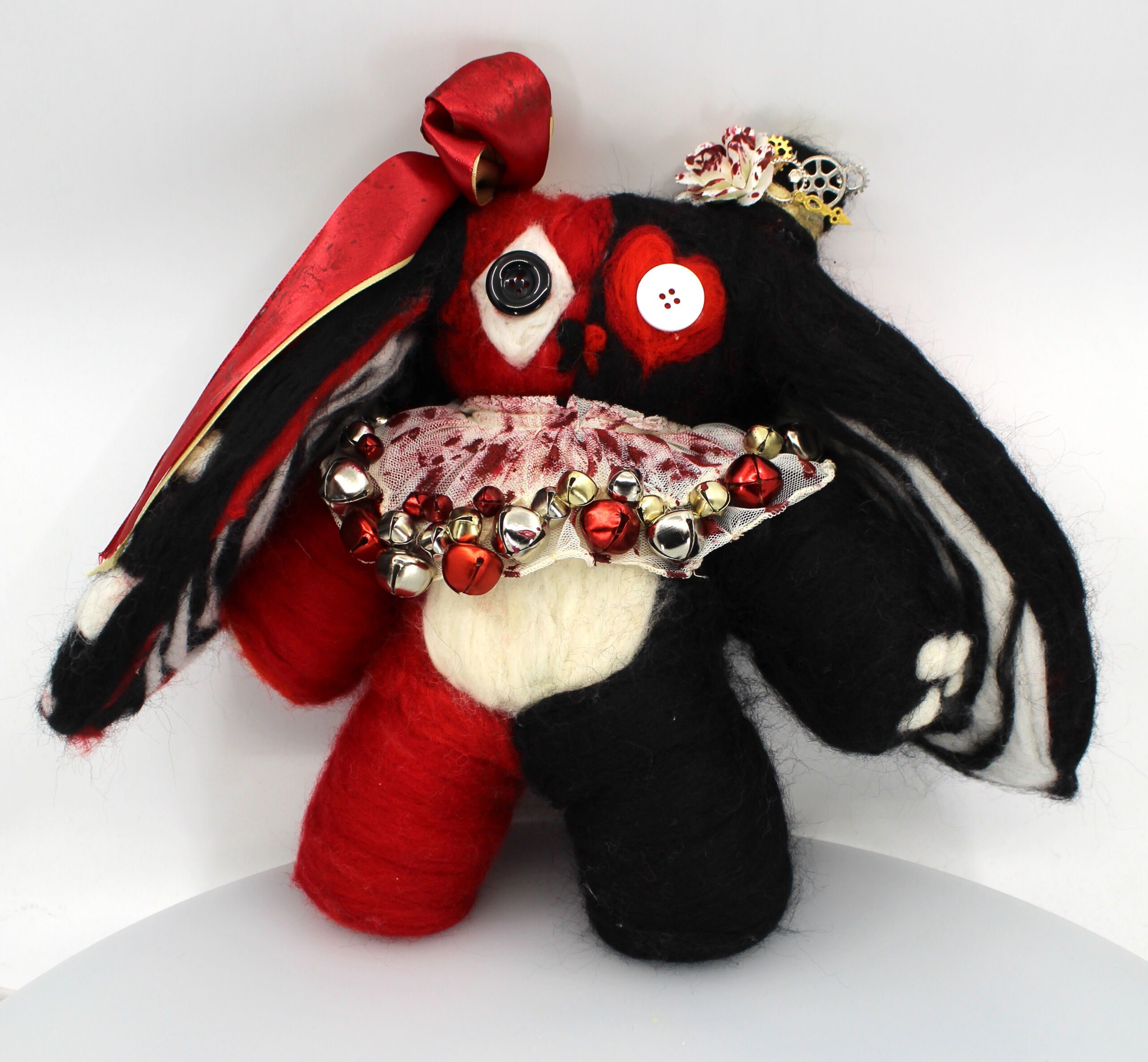 This image shows a needle-felted black, red, and white bunny plushies. The plushie looks like a Queen of Hearts card with a jester collar covered in blood stains and jingle bells. This is an art piece by Jocelyn Olguin, a student at Pritzker College Prep.