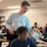 Cameron Forsythe is in his classroom talking to a student, standing beside him and pointing at the computer. They both are looking at the computer.