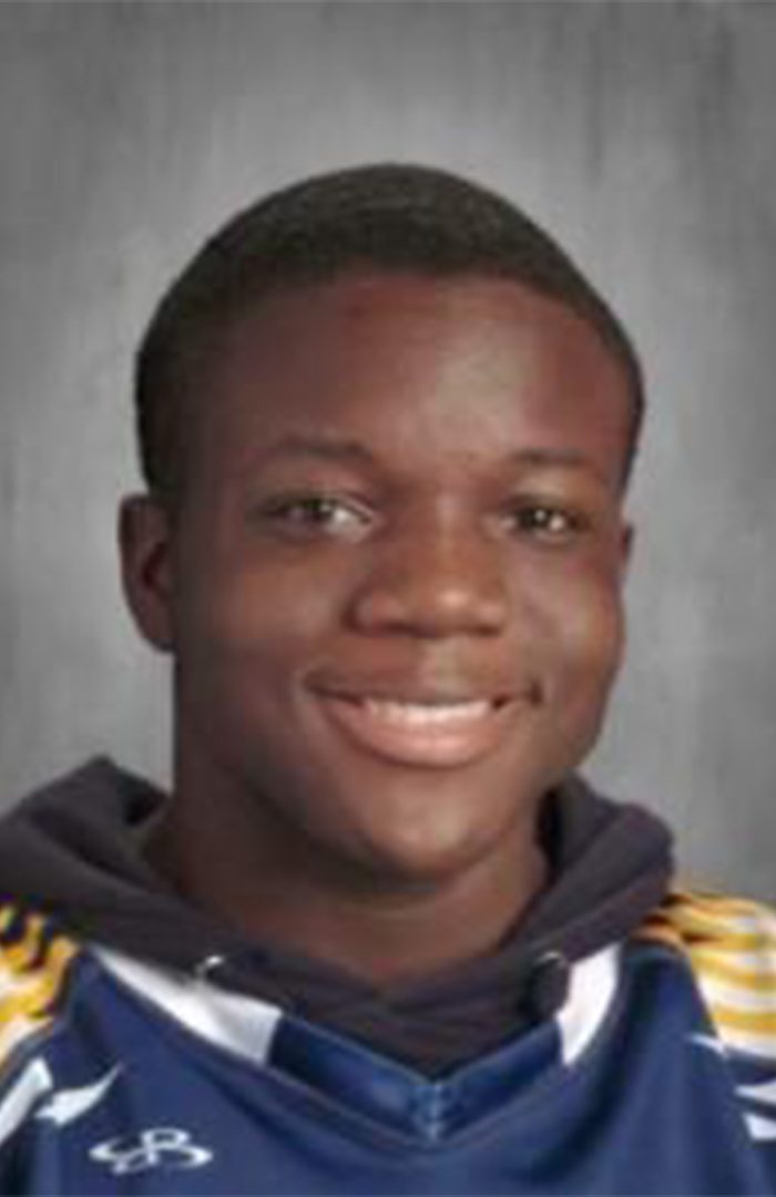 This photo is a headshot of Charles Williams, a student at Rauner College Prep. He is a young Black man with short hair. In this photo, he is smiling and wearing a sports jersey over a black hoodie.