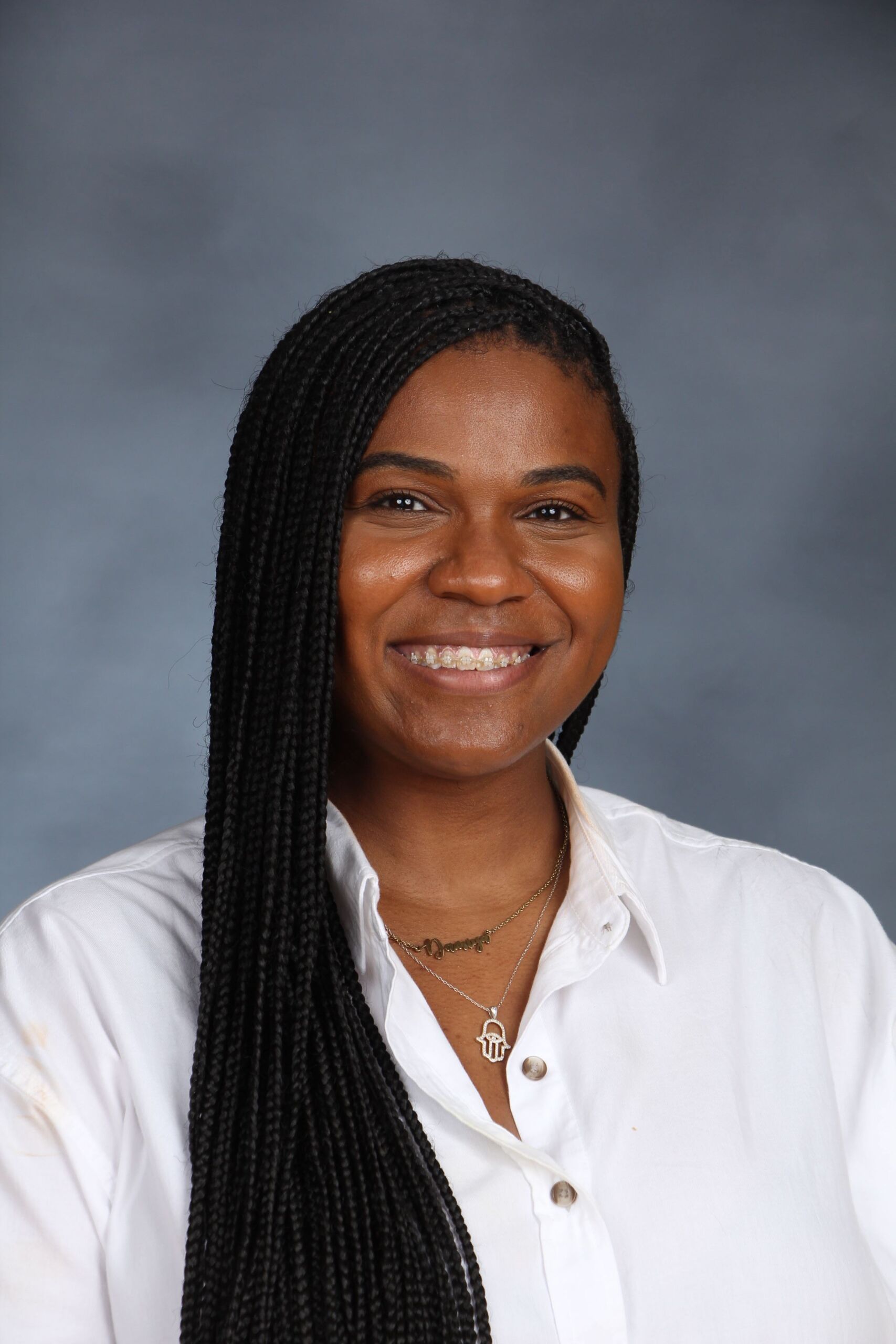Damiya Perkins in a professional headshot. She is smiling, has braids, and wearing a white button up.