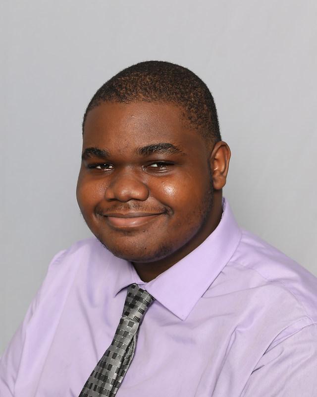 Photo shows a headshot of Patrick Okechukwu, a student at Hansberry College Prep. He is a young Black man with a short buzz cut. In this photo, he is smiling and wearing a pale purple button-up and silver tie.