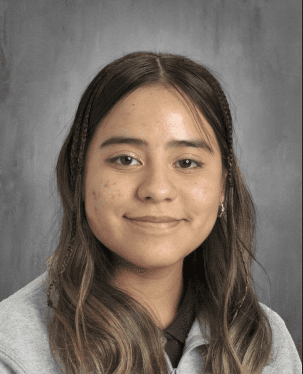 This photo is a headshot of Sandy Lopez, a student at Rowe-Clark Math & Science Academy. She is a young Latine woman with long wavy hair. In this photo, she is smiling and wearing a gray jacket over a black polo shirt.