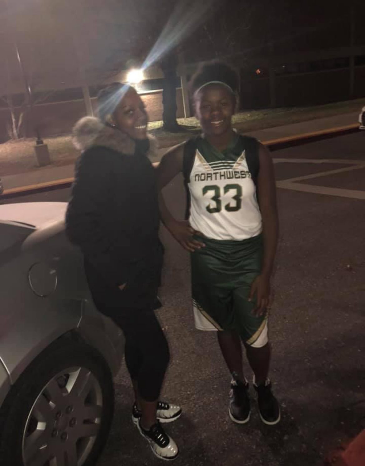 Photo shows Serenity in a basketball uniform, smiling next to her sister Sharde, outside in a parking lot after a game.