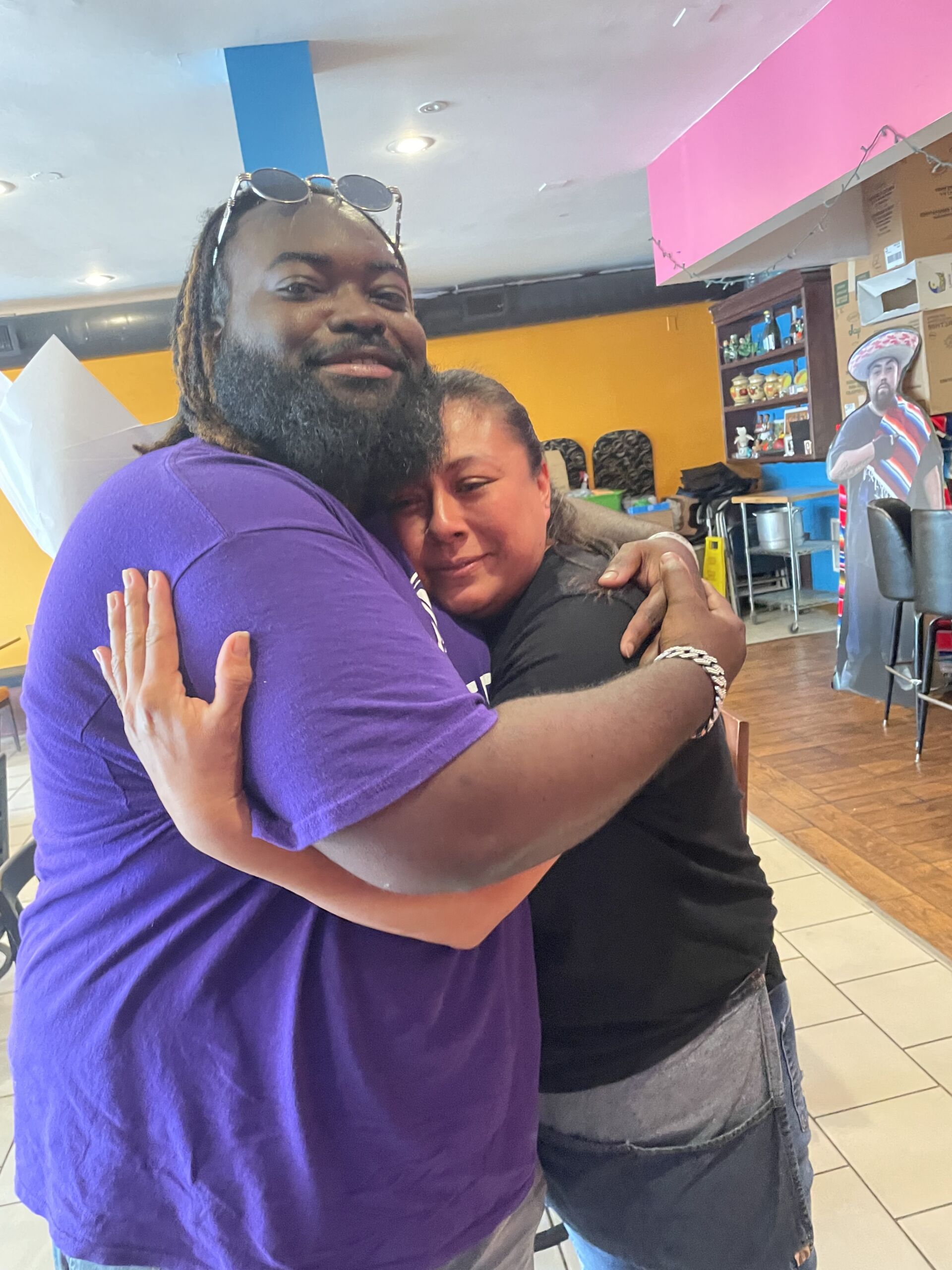 Photo shows Golder College Prep's band director Laurente Oby hugging Myrna Mendia, a parent at Golder. They are standing in the Mendia family's restaurant El Tezcal.