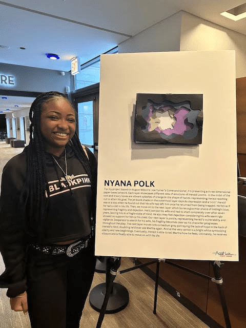 DRW student, Nyana Polk stands smiling beside her work
