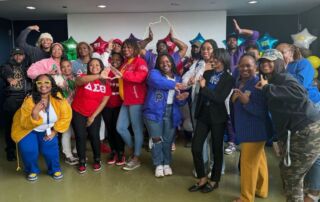 Gary Comer staff pose for a group photo on Greek Day. All of them are wearing their Greek Life swag. Many are making the sign for their sorority or fraternity with their arms.