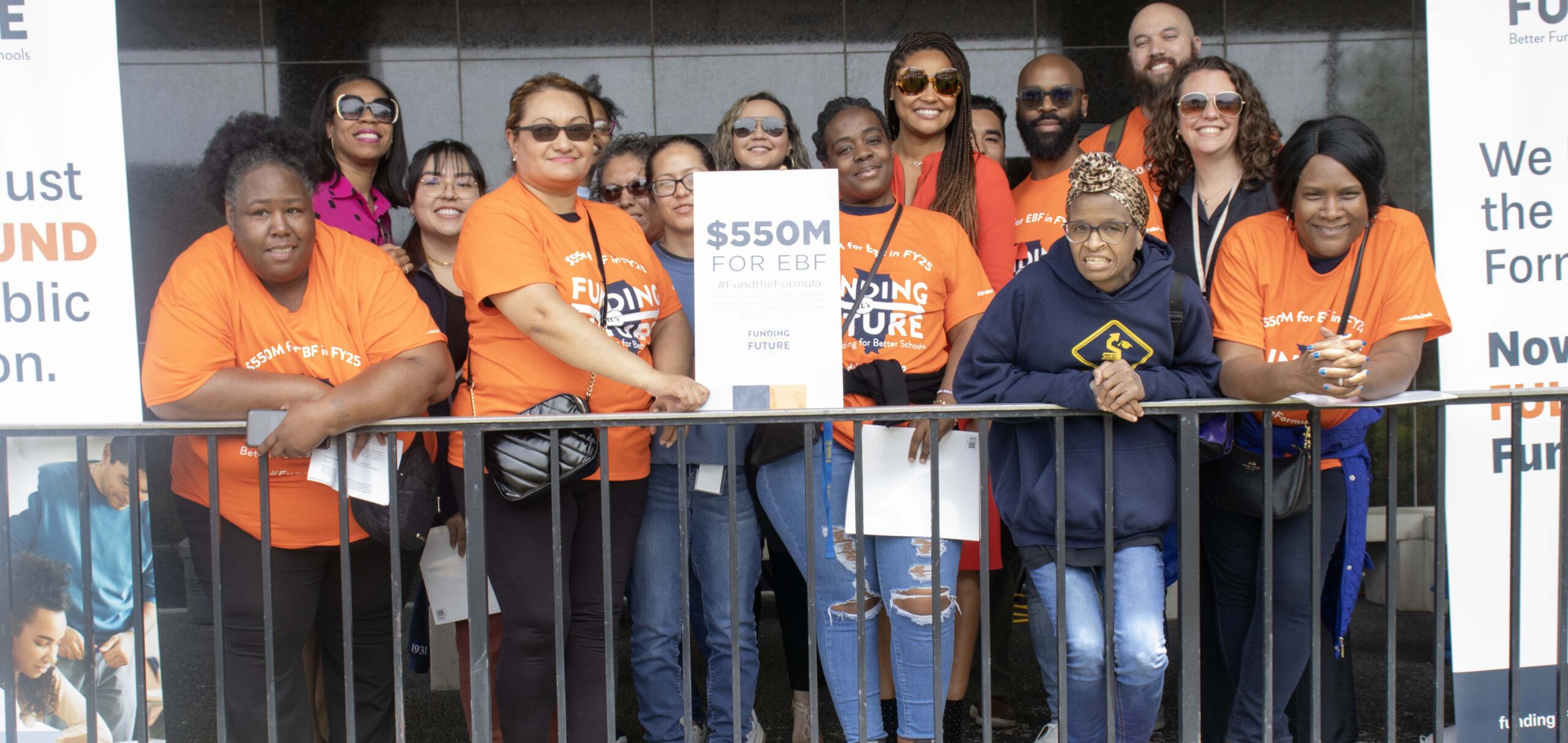 A contingent of Noble Schools' parents, alumni, and staff pose with posters calling for Evidence-Based Funding in Illinois. They are all wearing bright orange shirts that say Funding Illinois Future on it.