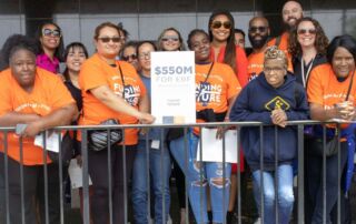 A contingent of Noble Schools' parents, alumni, and staff pose with posters calling for Evidence-Based Funding in Illinois. They are all wearing bright orange shirts that say Funding Illinois Future on it.