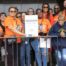 A contingent of Noble Schools' parents, alumni, and staff pose with posters calling for Evidence-Based Funding in Illinois. They are all wearing bright orange shirts that say Funding Illinois Future on it.