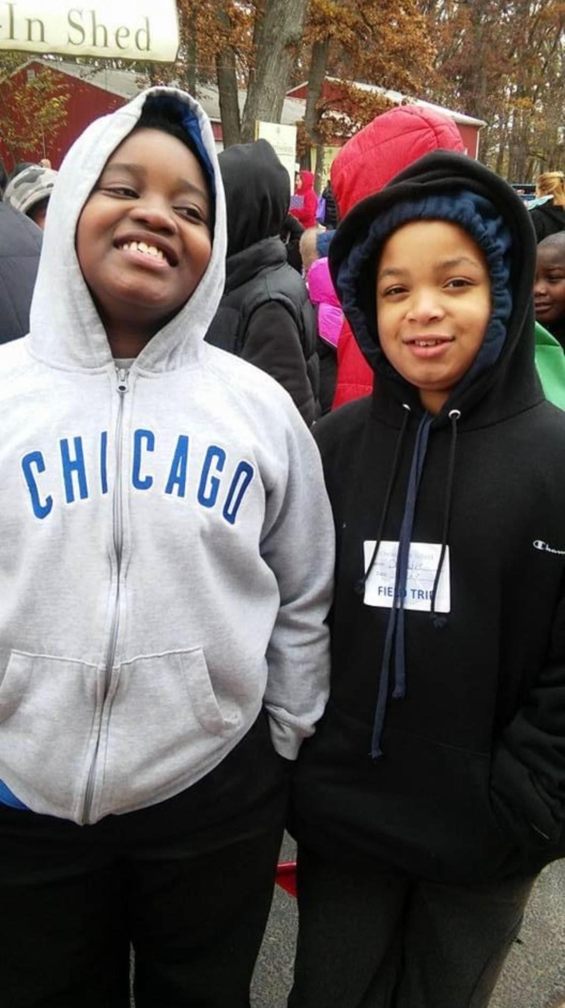 Two young Black boys wear hoodies and smile in the middle of a crowd outside. This is a photo of Deandre and Walter when they were much younger.