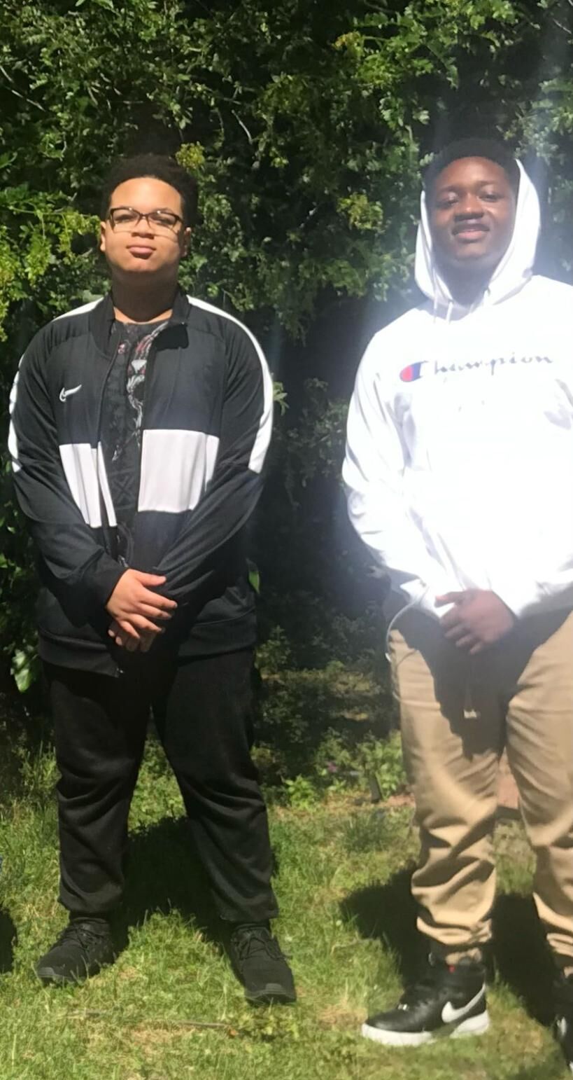 Two young Black high schoolers stand next to each other outside, both wearing jackets and slightly crossing their arms in front of their pelvis. This is a more recent photo of Deandre and Walter.