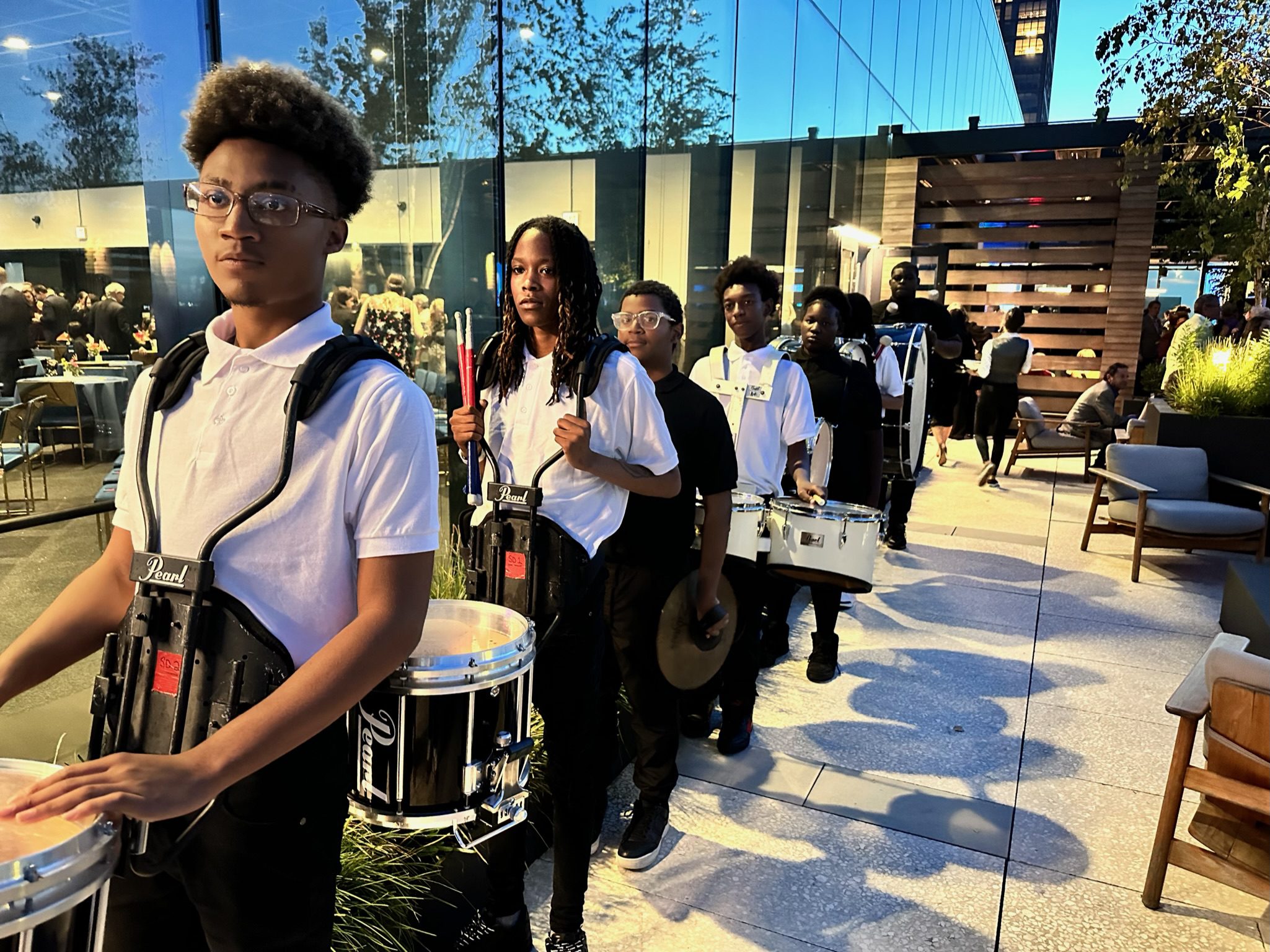 Johnson College Prep marching band students are carrying their instruments in a line down a sidewalk outside. They have just performed at Johnson's Homecoming.