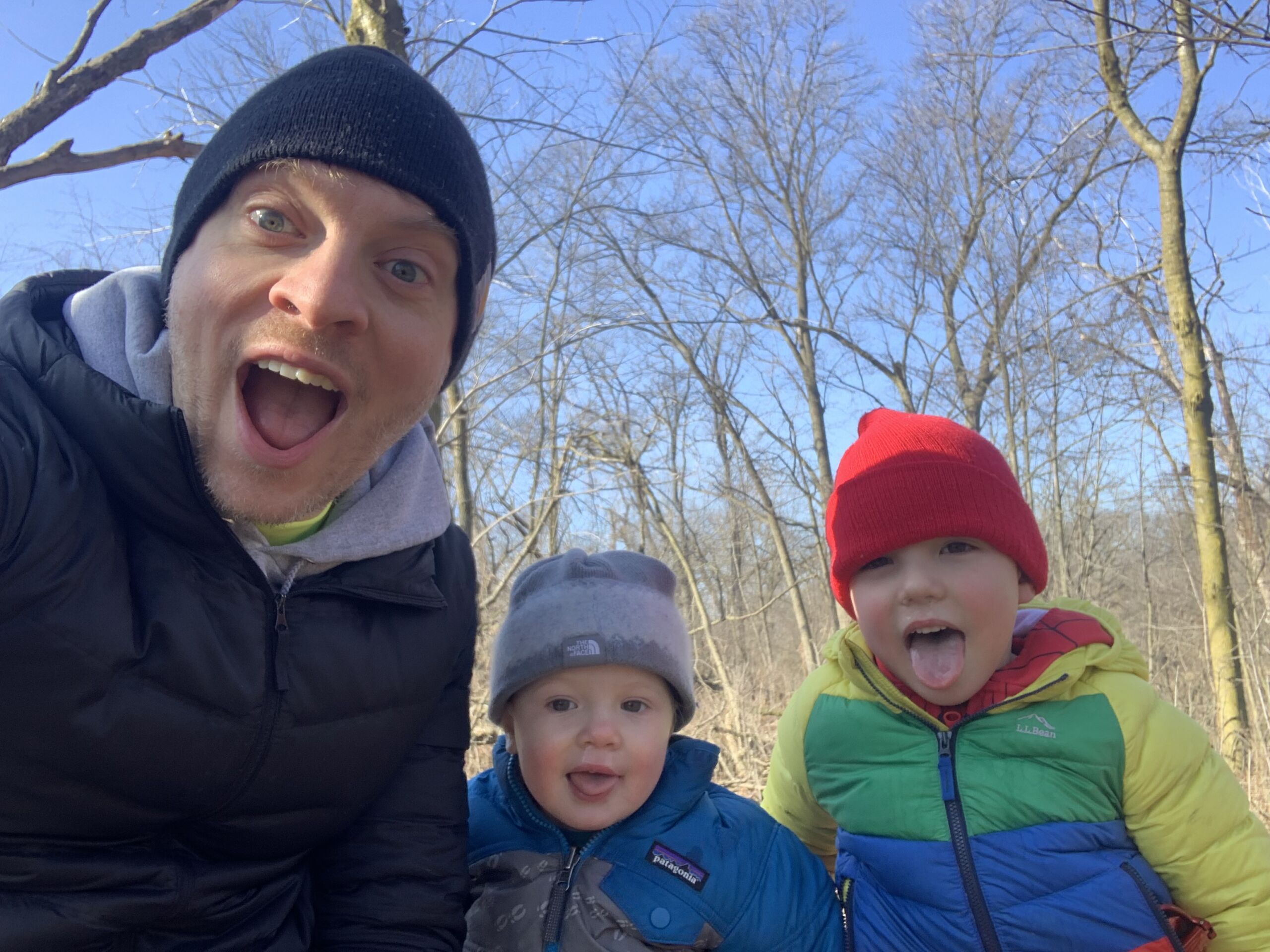 Gunty with his two small kids outside on a cold day. They are wearing hats and jackets and smiling.