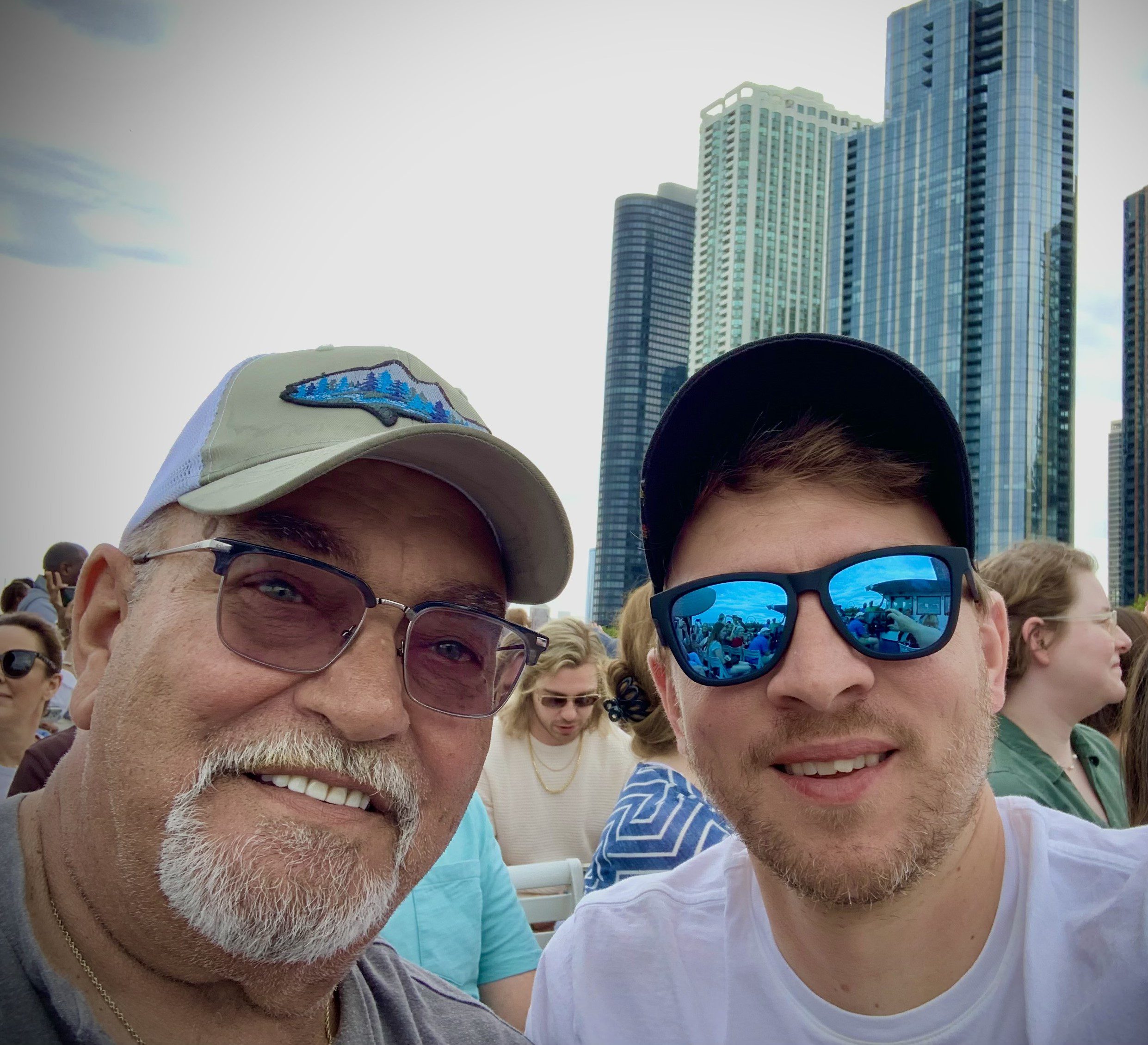 Selfie of Gunty and a family member smiling outside in front of a cloudy city skyline.