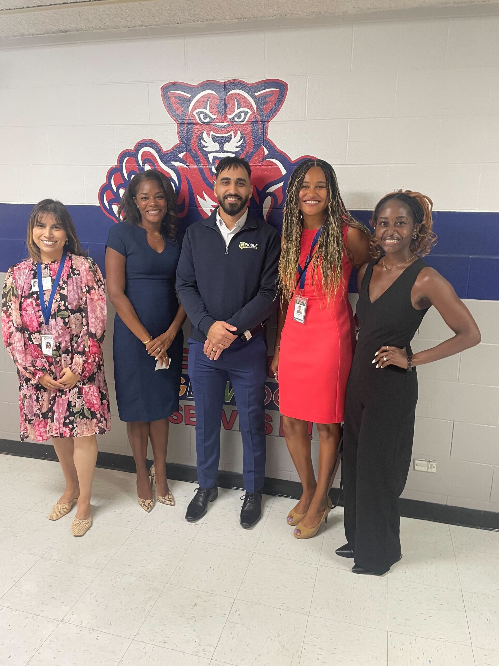 Salameh with Noble CEO Constance Jones and other school staff. They are posing in the Johnson hallway in front of a big decal of the Puma mascot.