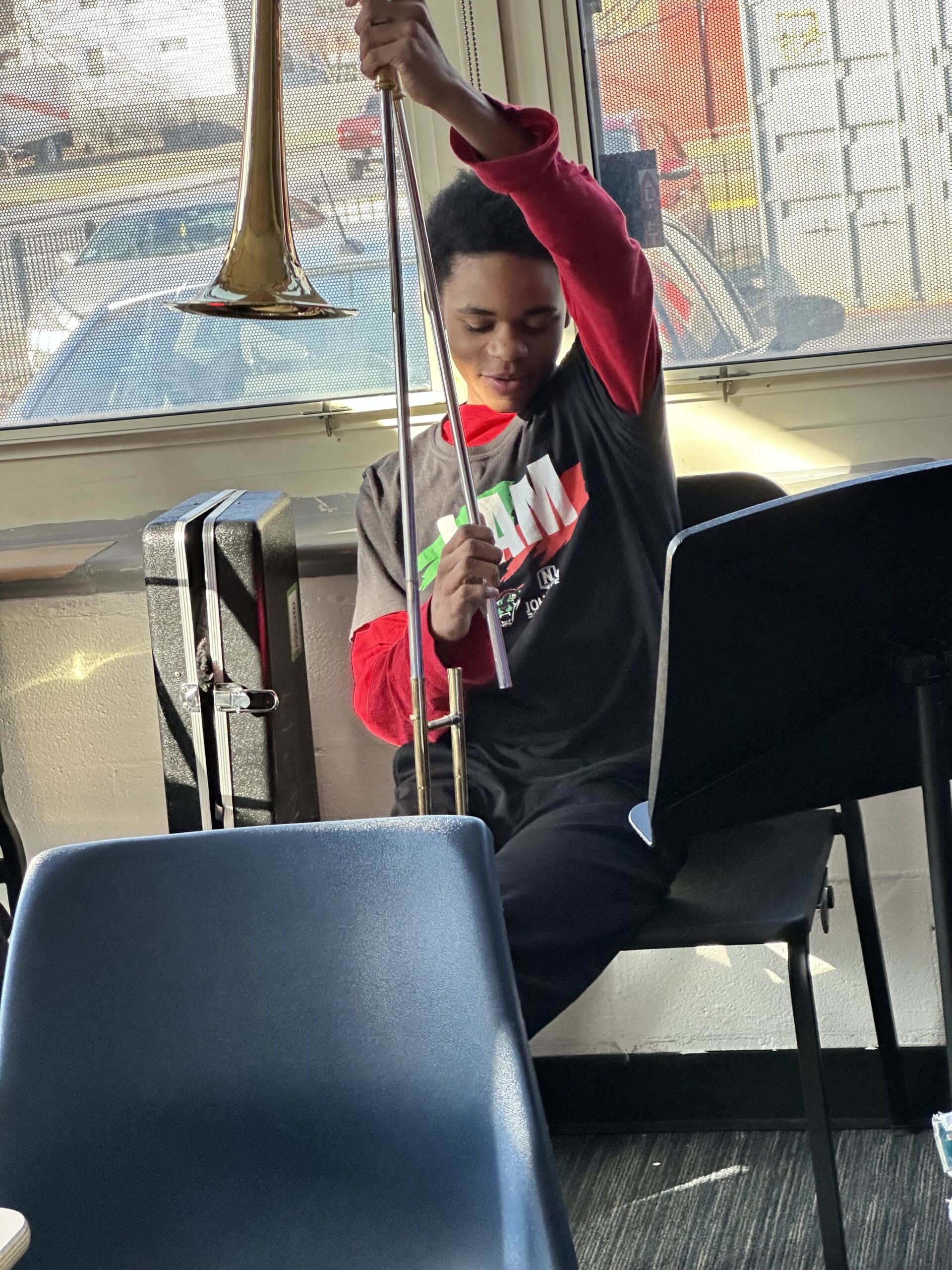 Karlito Franklin is sitting at a chair in the band room, putting together his trombone.