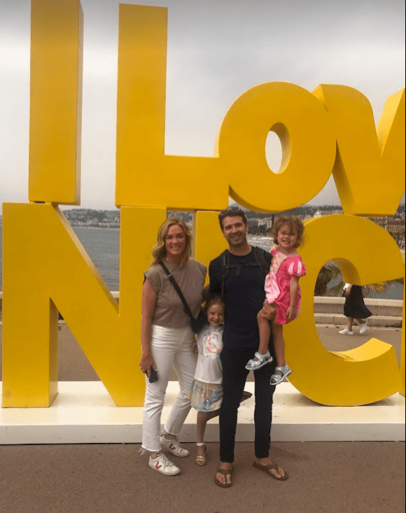 Lawrence with her family on vacation. They are outside and in front of a giant yellow sculpture that says "I love NIC"