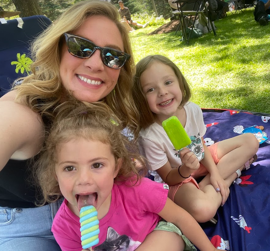 Lawrence outside on a picnic with her two small children. They both are eating popsicles.