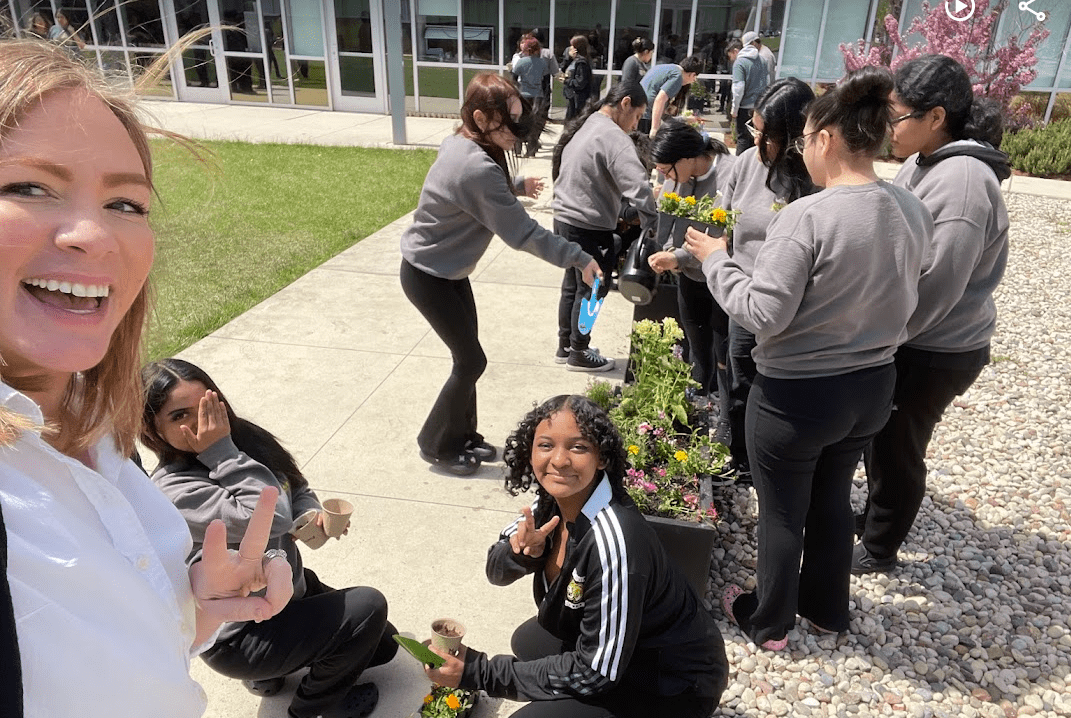 A selfie of Lawrence outside on the Mansueto campus with students. They are planting flowers along the walkway.